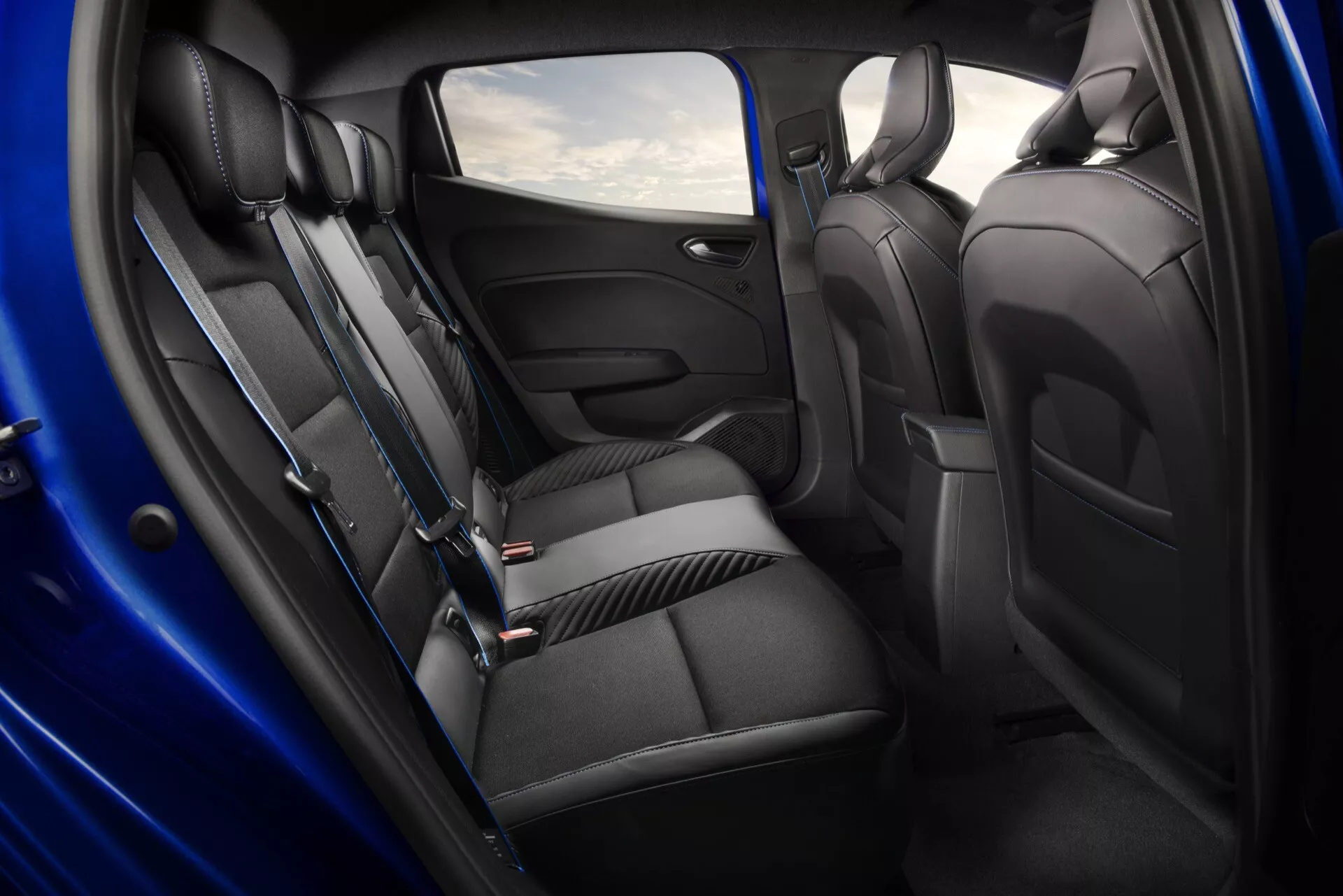 Intérieur du Renault Clio V-facelift 2023 présentant le compartiment passager arrière avec des sièges haut de gamme, un accoudoir pliable et des fonctionnalités avancées pour le confort et la commodité, vu sous un angle de porte ouverte