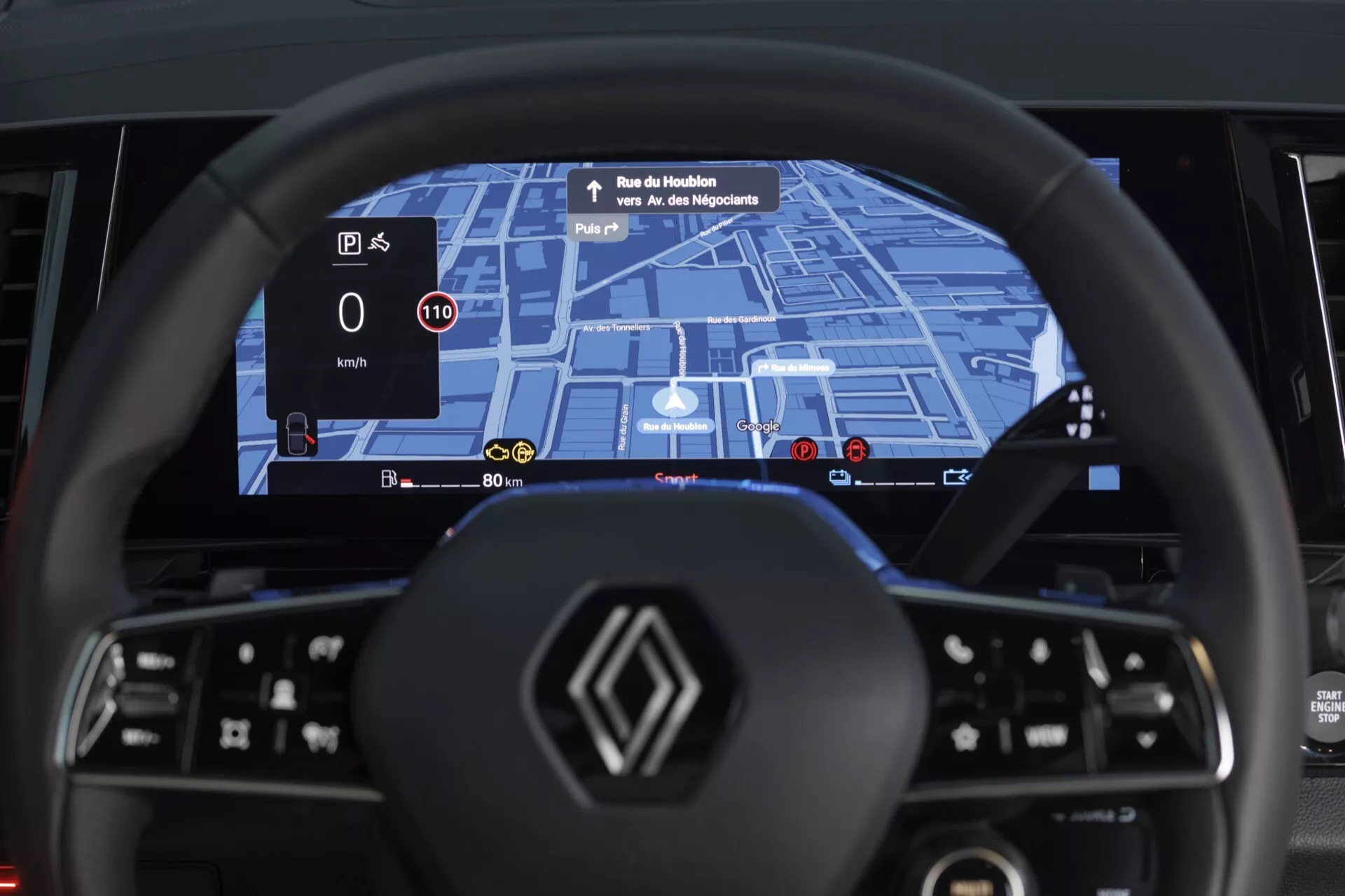 Vue intérieure du Renault Espace VI 2023 depuis le siège du conducteur mettant en avant le volant moderne à fond plat avec commandes multifonctions et le tableau de bord digital large écran avec navigation GPS intégrée, détection de la limite de vitesse et affichage du niveau d'énergie pour une motorisation hybride ou électrique, plus un HUD projetant la vitesse et les instructions de navigation