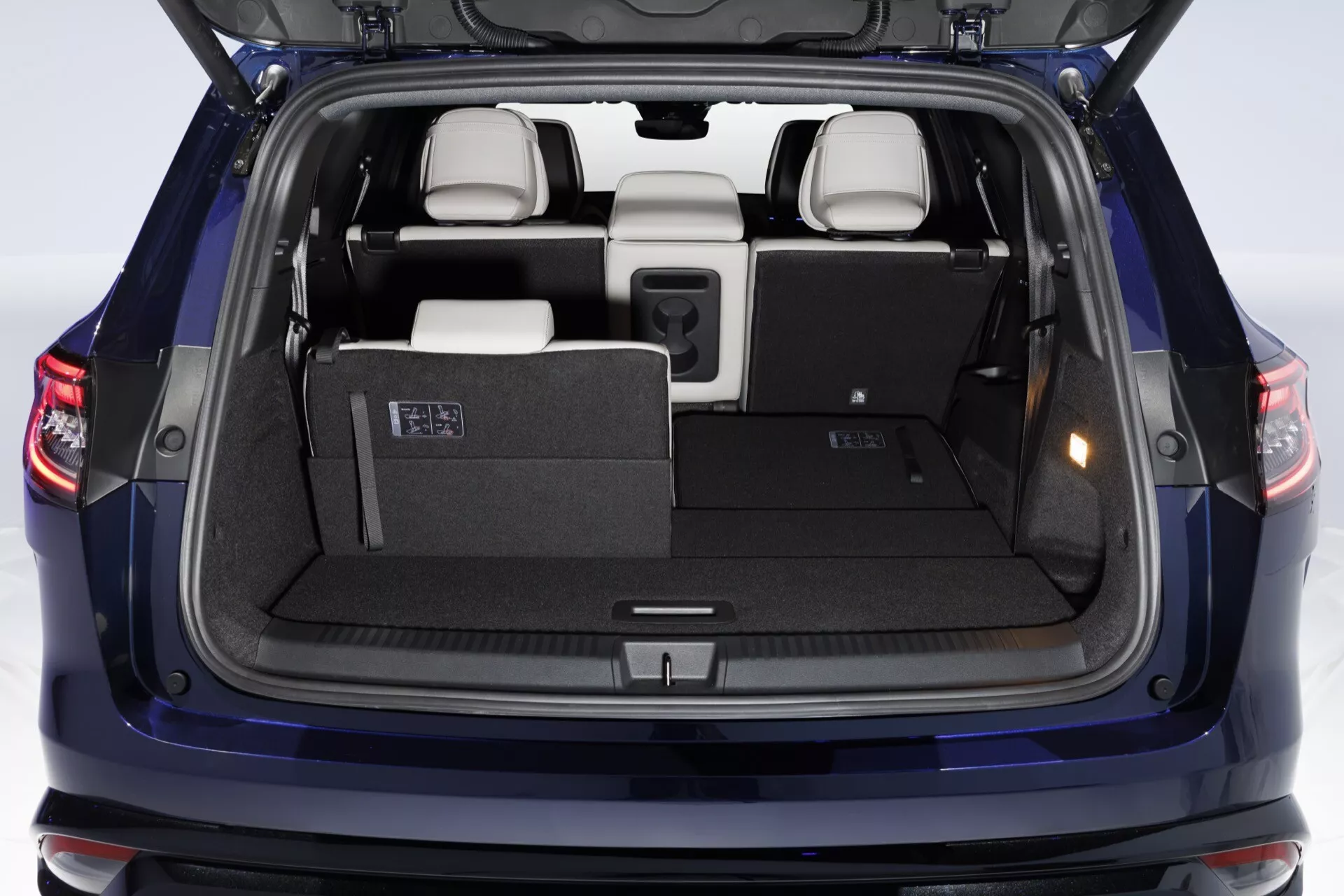 Renault Espace VI 2023 présentant une vue arrière avec hayon de chargement ouvert, mettant en évidence un coffre spacieux, feux arrière LED, sièges de troisième rangée rabattables, matériaux intérieurs de haute qualité, leviers de configuration des sièges faciles à utiliser, couverture de confidentialité, doublure détaillée du hayon et capteurs de stationnement