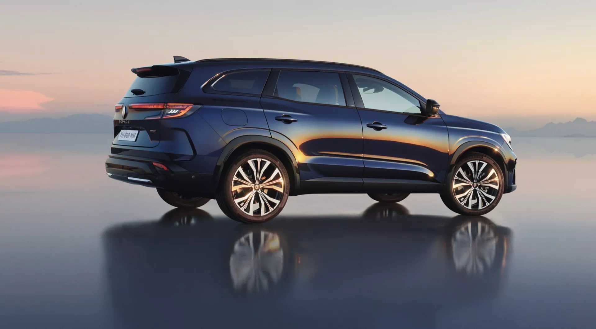 Vue de profil à angle moyen du Renault Espace VI 2023, présentant le design de luxe du SUV avec des barres de toit, des feux arrière LED, un becquet arrière, un échappement double et des jantes en alliage à plusieurs branches axées sur l'utilité et l'aventure, le tout contre un horizon numériquement rendu se reflétant sur une surface lisse.