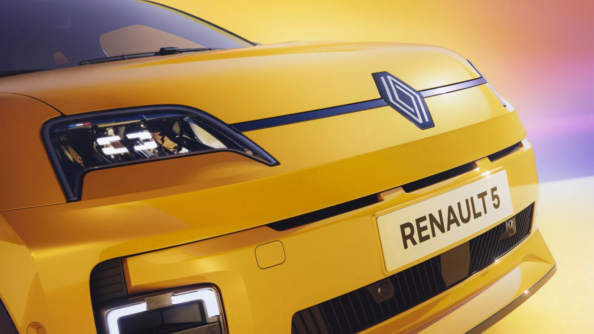 Gros plan sur le devant de la Renault R5 2024 présentant une peinture jaune métallique, un logo en forme de diamant, des phares LED et des feux de jour à LED avec une grille fermée moderne suggérant une technologie électrique, sous un angle ascendant puissant soulignant les éléments de marque et de conception