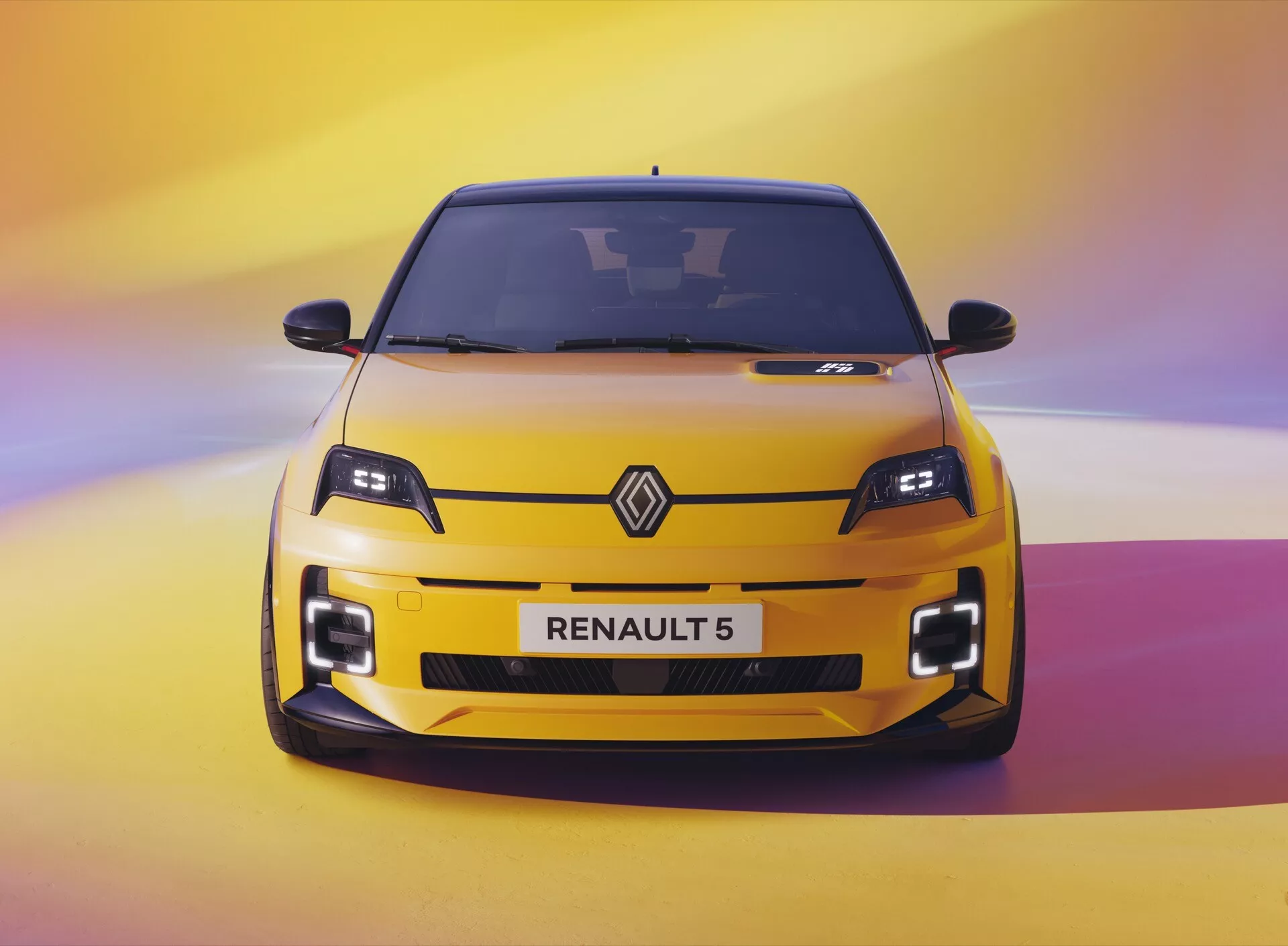 Vue de face vibrante d'une Renault 5 de 2024 en jaune vif sur un fond dégradé de violet à jaune, soulignant ses phares LED modernes, les grandes prises d'air sur le pare-chocs et le design sportif.