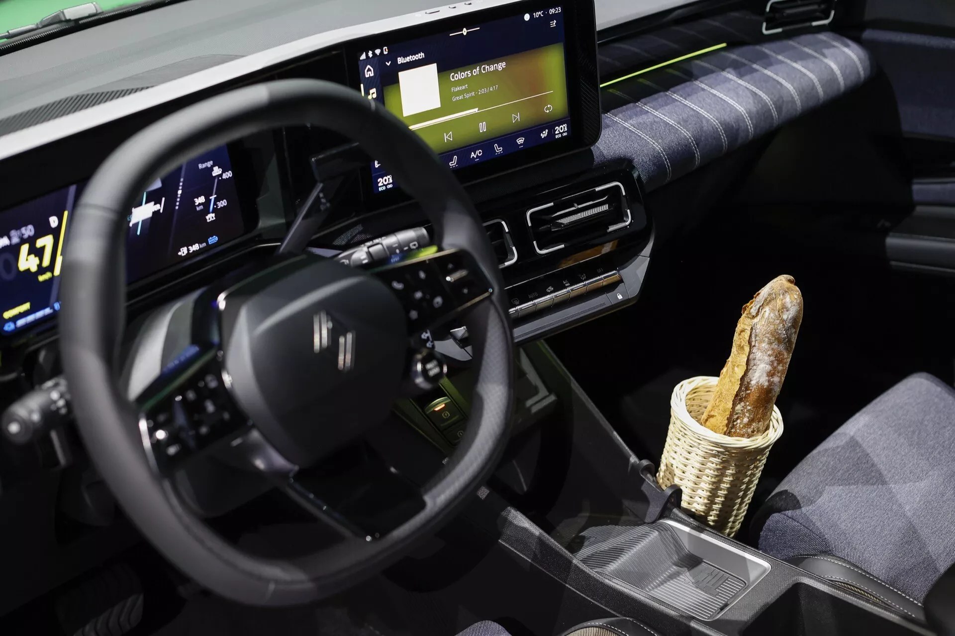 Intérieur du Renault R5 2024 présentant un volant multifonctionnel avec un design à fond plat, un large cluster d'instruments numériques indiquant le statut du véhicule électrique tel que la vitesse et l'autonomie de la batterie, un écran tactile central d'infodivertissement avec des fonctionnalités de connectivité, et une touche d'humour avec une baguette dans le rangement de la console centrale, incarnant la conception et la technologie modernes du véhicule