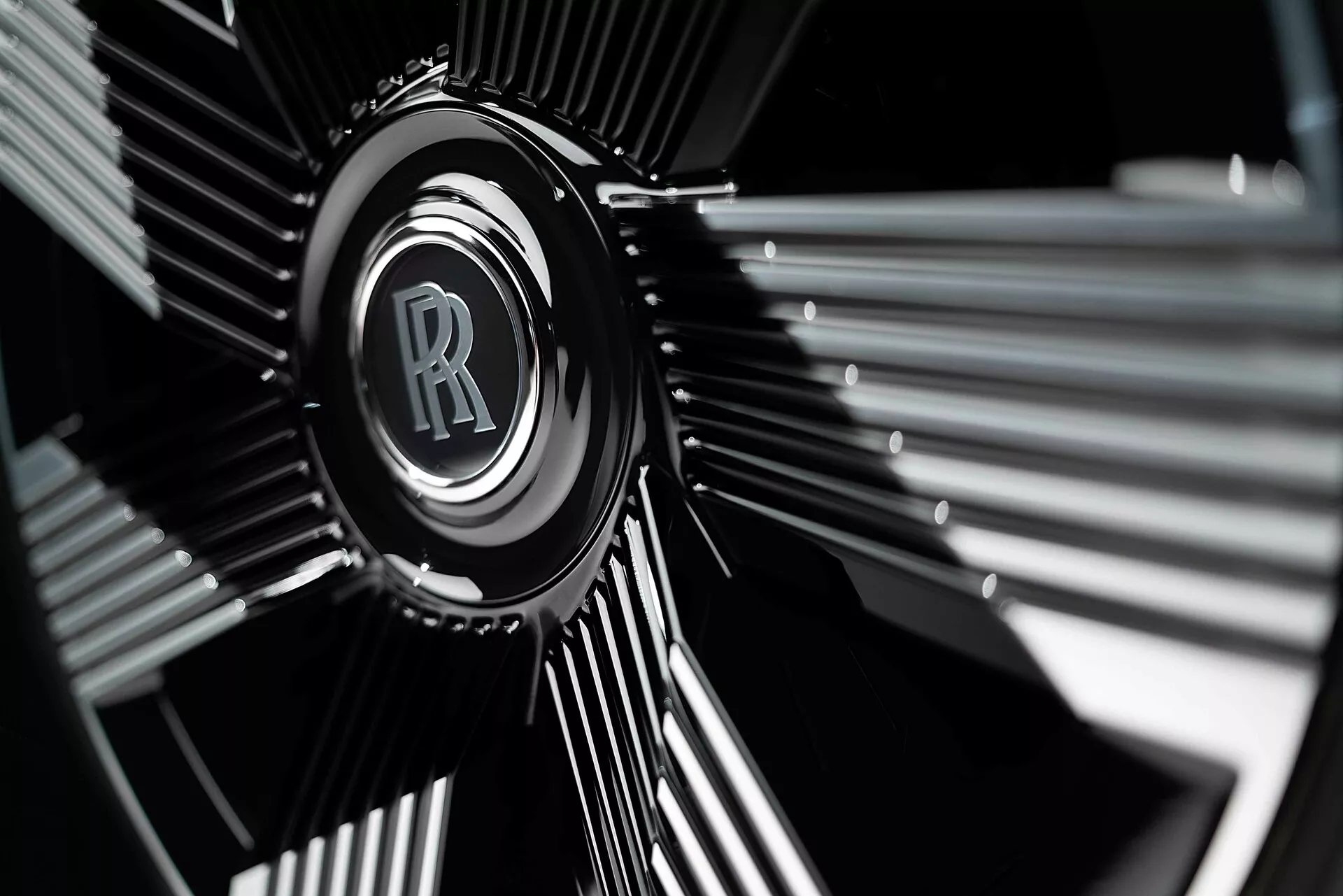 Détail du bord de roue de la Rolls-Royce Spectre de première génération 2023 avec l'emblème iconique RR en chrome sur un design sombre à plusieurs branches, mis en évidence par la photographie à faible profondeur de champ