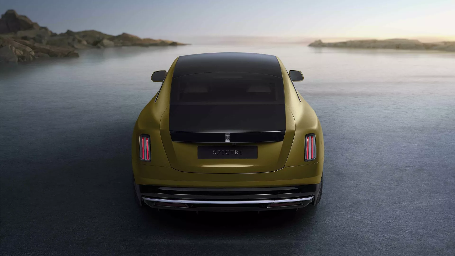 Rolls-Royce Spectre 1ère génération 2023 en or métallisé capturée depuis une perspective arrière à l'heure dorée, mettant en évidence ses feux arrière LED, design aérodynamique du coffre, pare-chocs arrière poli, système d'échappement double et positionnée contre un fond côtier tranquille.