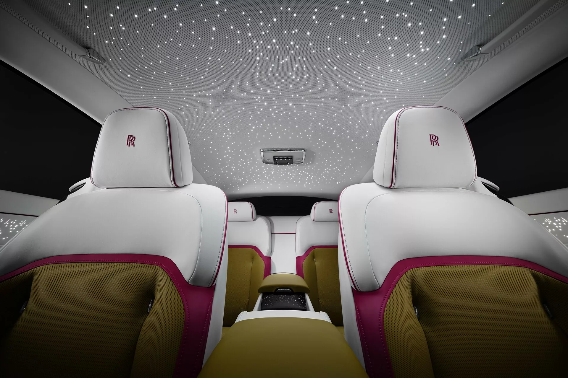 Intérieur luxueux de la Rolls-Royce Spectre 2023 de première génération, sièges arrière en cuir blanc avec détails magenta, logo Rolls-Royce sur les appuie-têtes et ciel étoilé au plafond