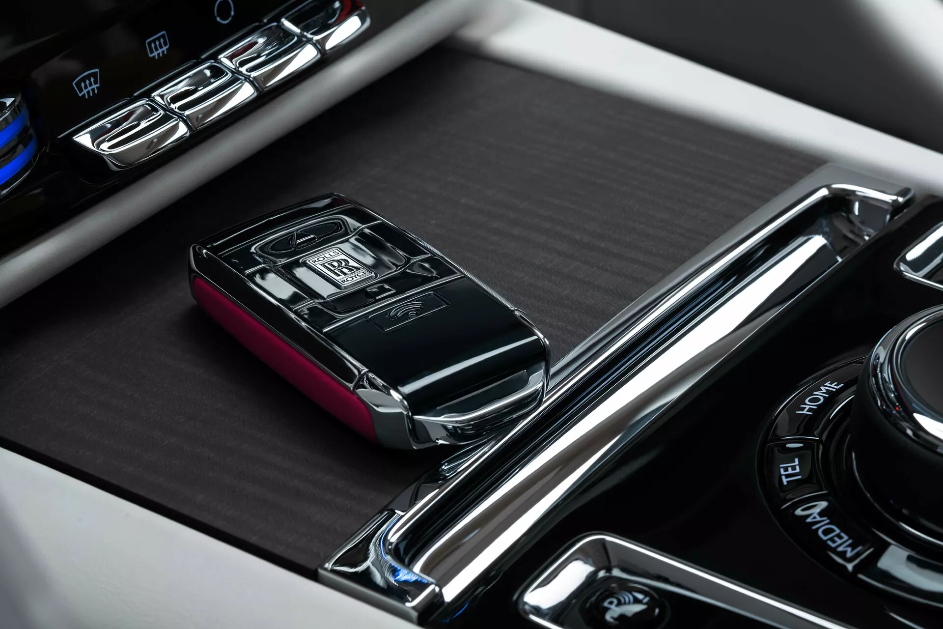 Gros plan sur la console centrale de la Rolls-Royce Spectre 2023 avec un focus sur le porte-clés de la voiture de luxe dans son emplacement désigné, entouré de garniture chromée et à côté de boutons de commande illuminés et d'un cadran multimédia rotatif.