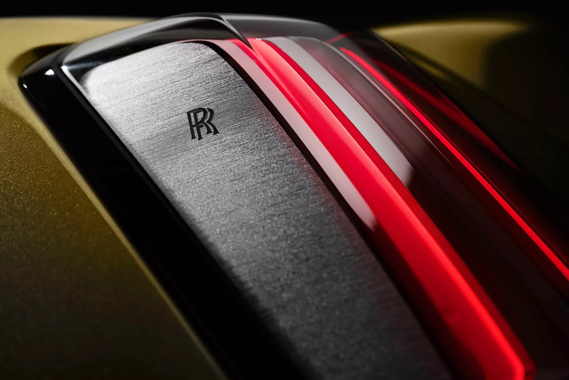 Vue rapprochée du capot de la Rolls-Royce Spectre 2023 avec des doubles bandes rouges, l'emblème double 'R' iconique et une finition dorée luxueuse