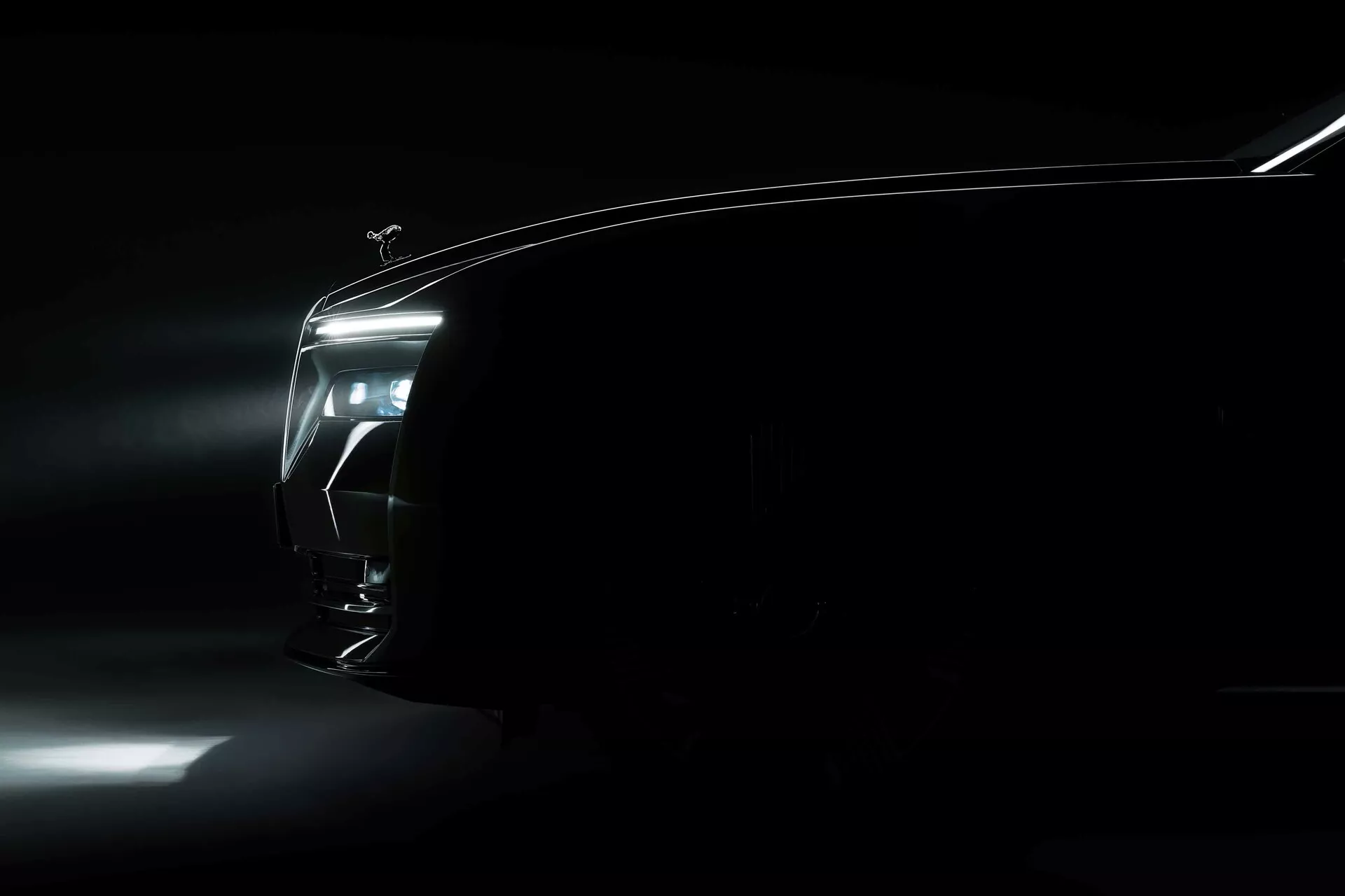 Rolls-Royce Spectre 1ère génération 2023 dans un éclairage dramatique faible mettant en valeur la silhouette et l'éclairage, avec un accent sur la conception du phare LED et l'aérodynamique élégante du quart avant