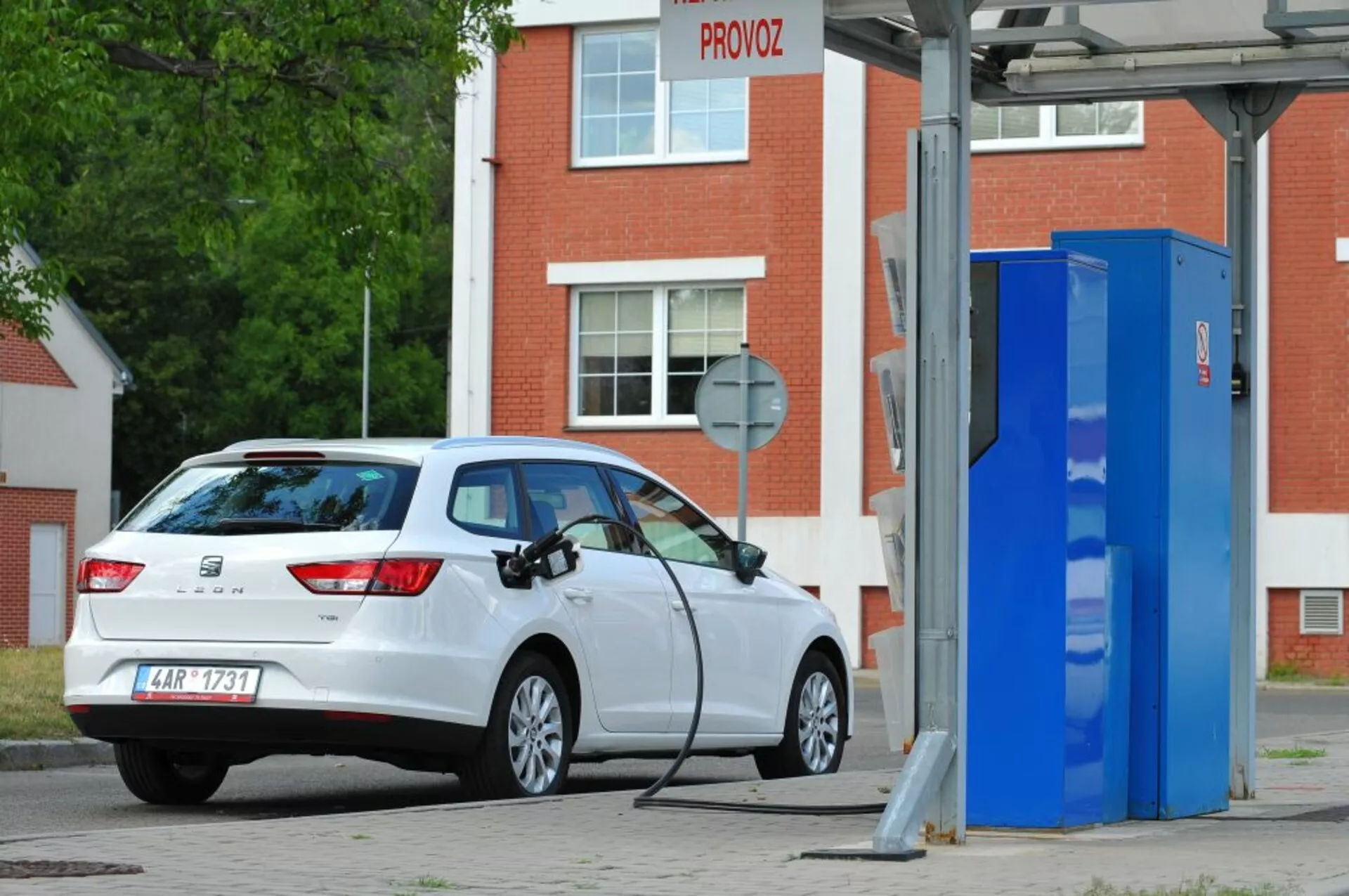 Voiture hatchback blanche Seat Leon SC de 2016, électrique ou hybride rechargeable, garée à une station de recharge pour véhicules électriques, montrant une vue arrière trois quarts mettant en évidence les feux arrière, le pare-brise arrière, le profil du hayon et le port de charge sur le côté droit