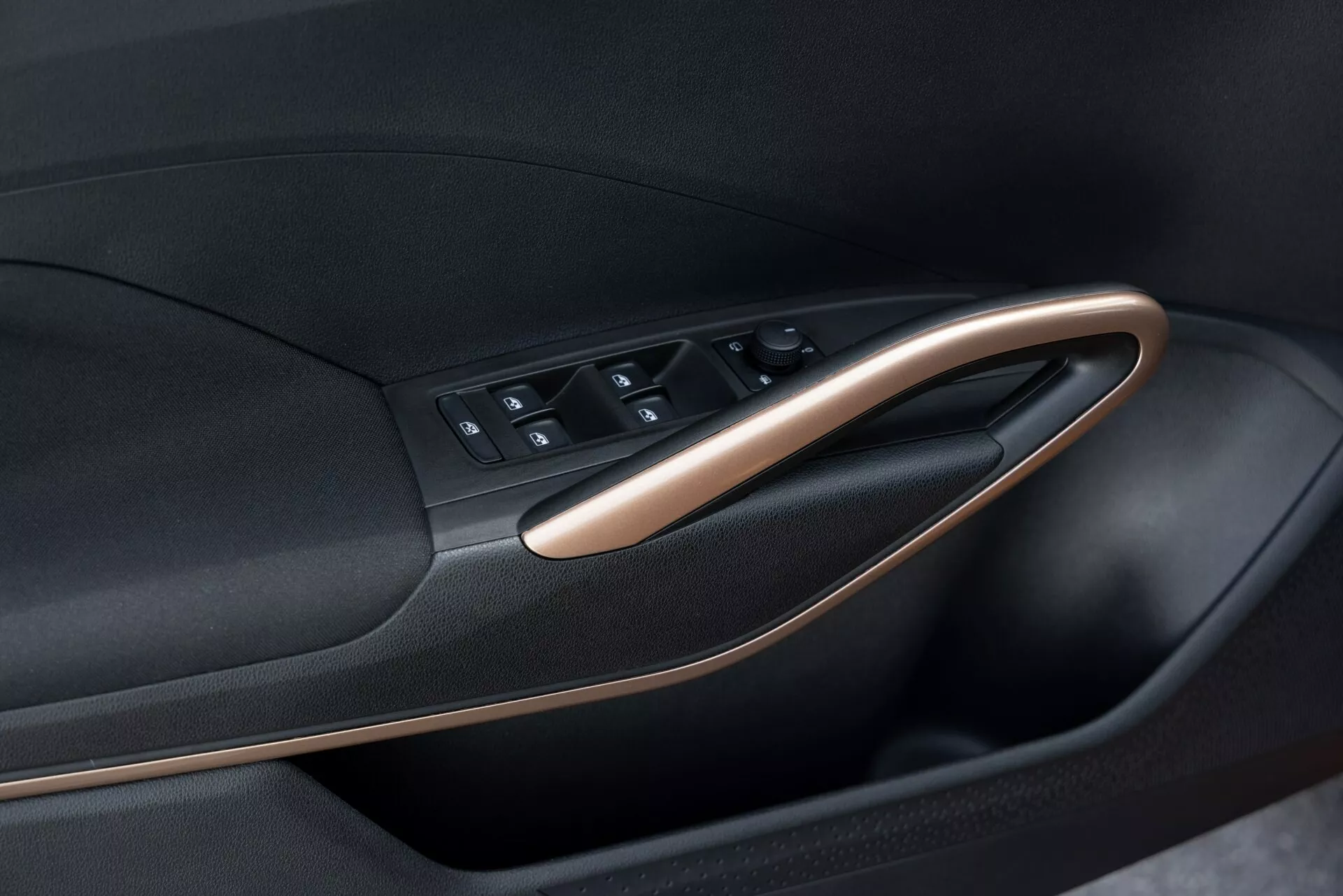 Gros plan sur le panneau de porte intérieur de la Skoda Fabia 2021, mettant en avant le module de commande de porte. L'image, prise sous un angle oblique, met en valeur la disposition des boutons et le contour de la porte. Le module de commande de porte comprend des boutons pour les commandes des fenêtres, les verrouillages de porte et peut-être les réglages des rétroviseurs. Le panneau présente un design bicolore avec un matériau noir accentué par des finitions métalliques ou en grain de bois, soulignant le design moderne et ergonomique de la voiture.