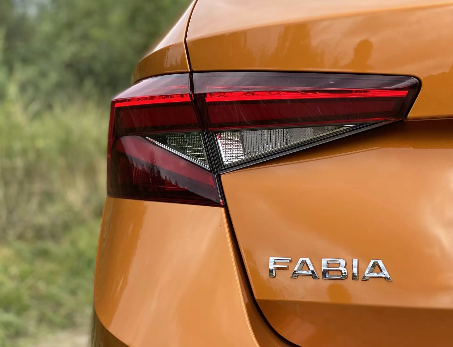 Image en gros plan du coin arrière d'une Skoda Fabia 2021 mettant en évidence le design angulaire et net de l'assemblage des feux arrière à LED et le marquage distinctif 'FABIA' sur la carrosserie métallique orange brillant. Les courbes lisses et les légères bosses autour du feu arrière ajoutent à l'esthétique moderne, capturée sous un angle légèrement surélevé avec une faible profondeur de champ.