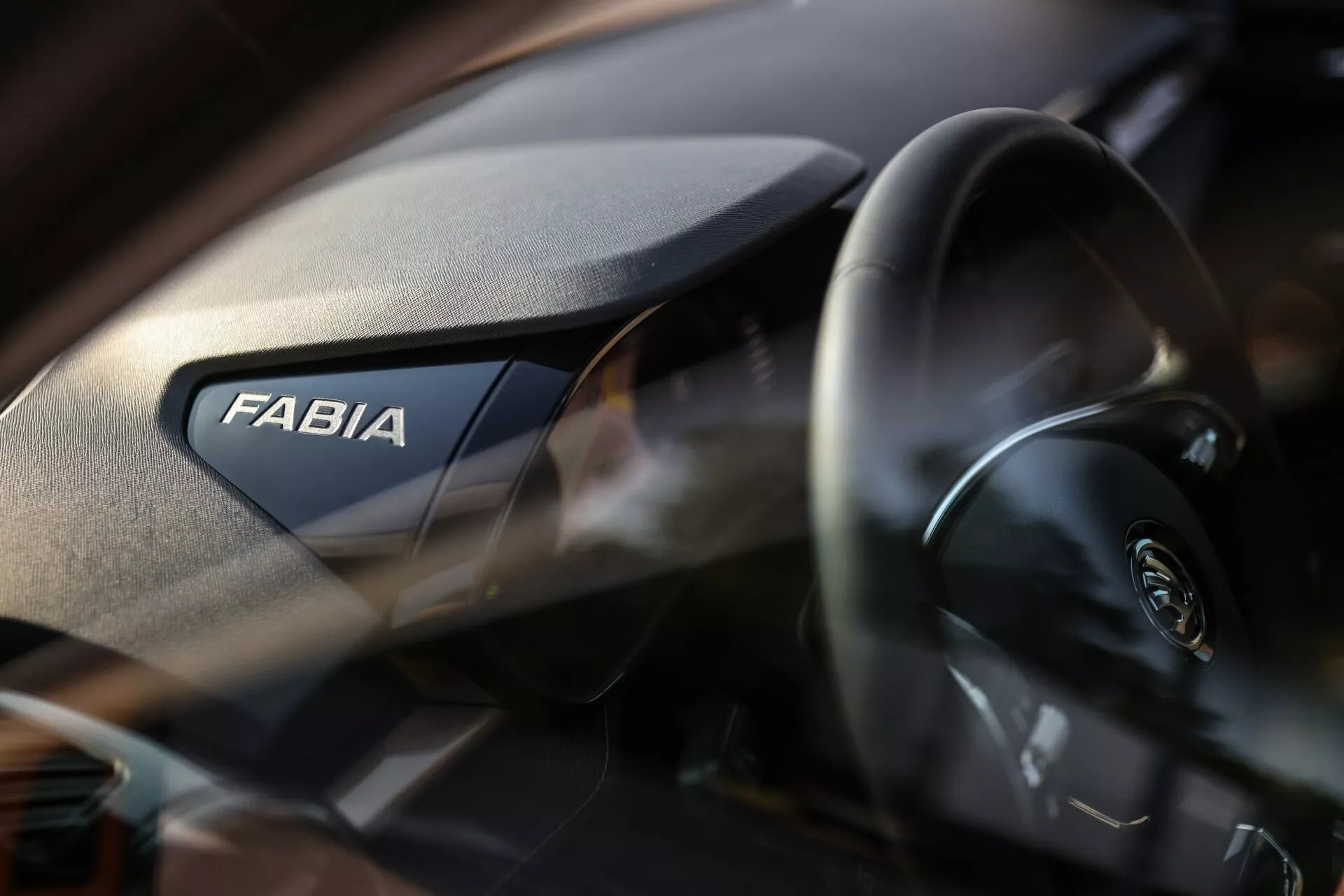 Vue intérieure rapprochée de la Skoda Fabia 2021, mettant en évidence le côté passager du tableau de bord. Le mot 'FABIA' est affiché en bonne place, tandis que le volant moderne avec le logo Skoda est partiellement visible à gauche. Le tableau de bord présente une texture granuleuse et la profondeur de champ réduite met en valeur la marque avec un arrière-plan légèrement flou.