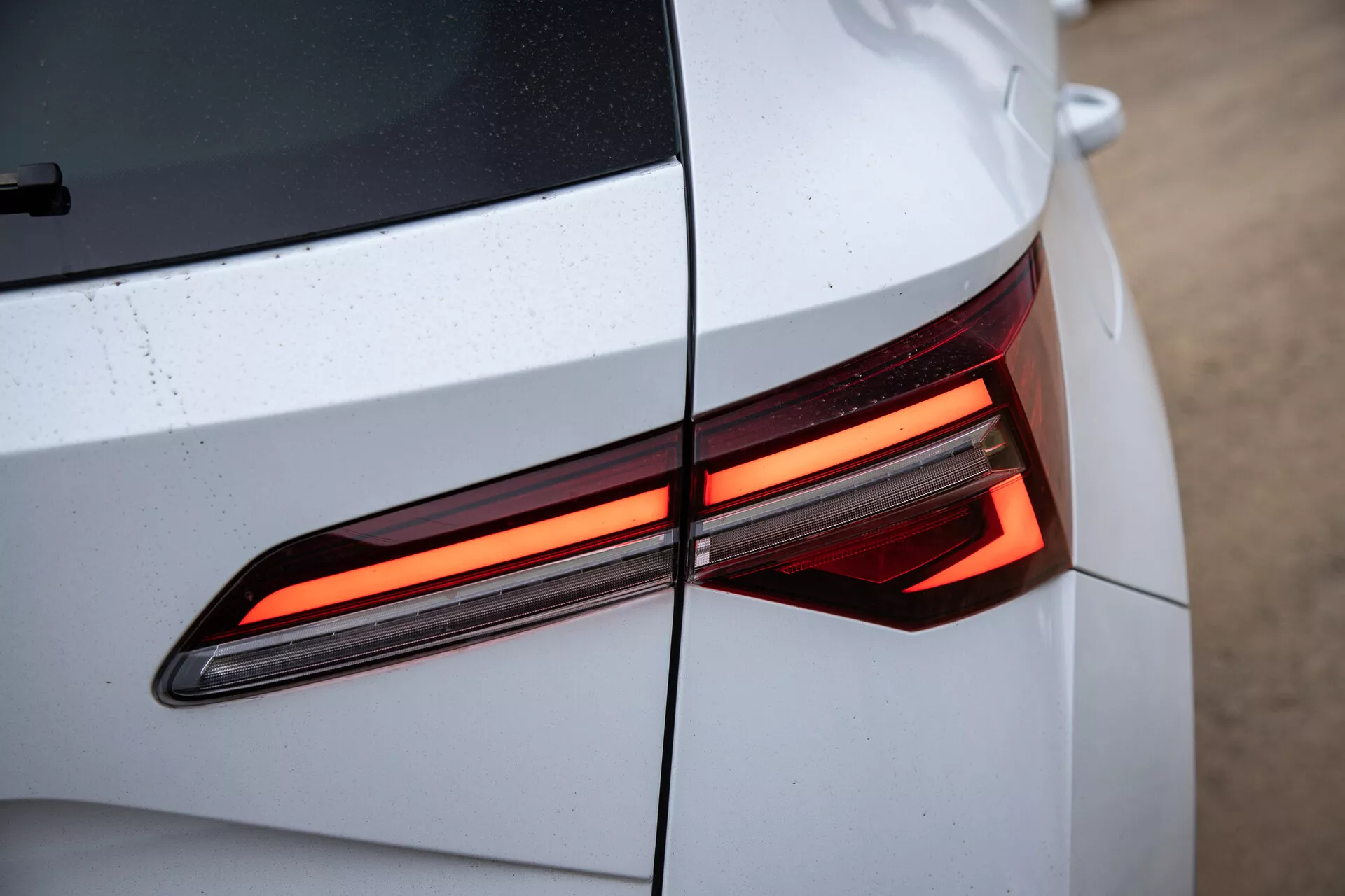 Gros plan sur la section arrière de la Skoda Karoq 2021 montrant le design moderne du feu arrière LED, avec un accent sur les lignes angulaires et la carrosserie brillante de couleur claire avec des gouttes d'eau visibles