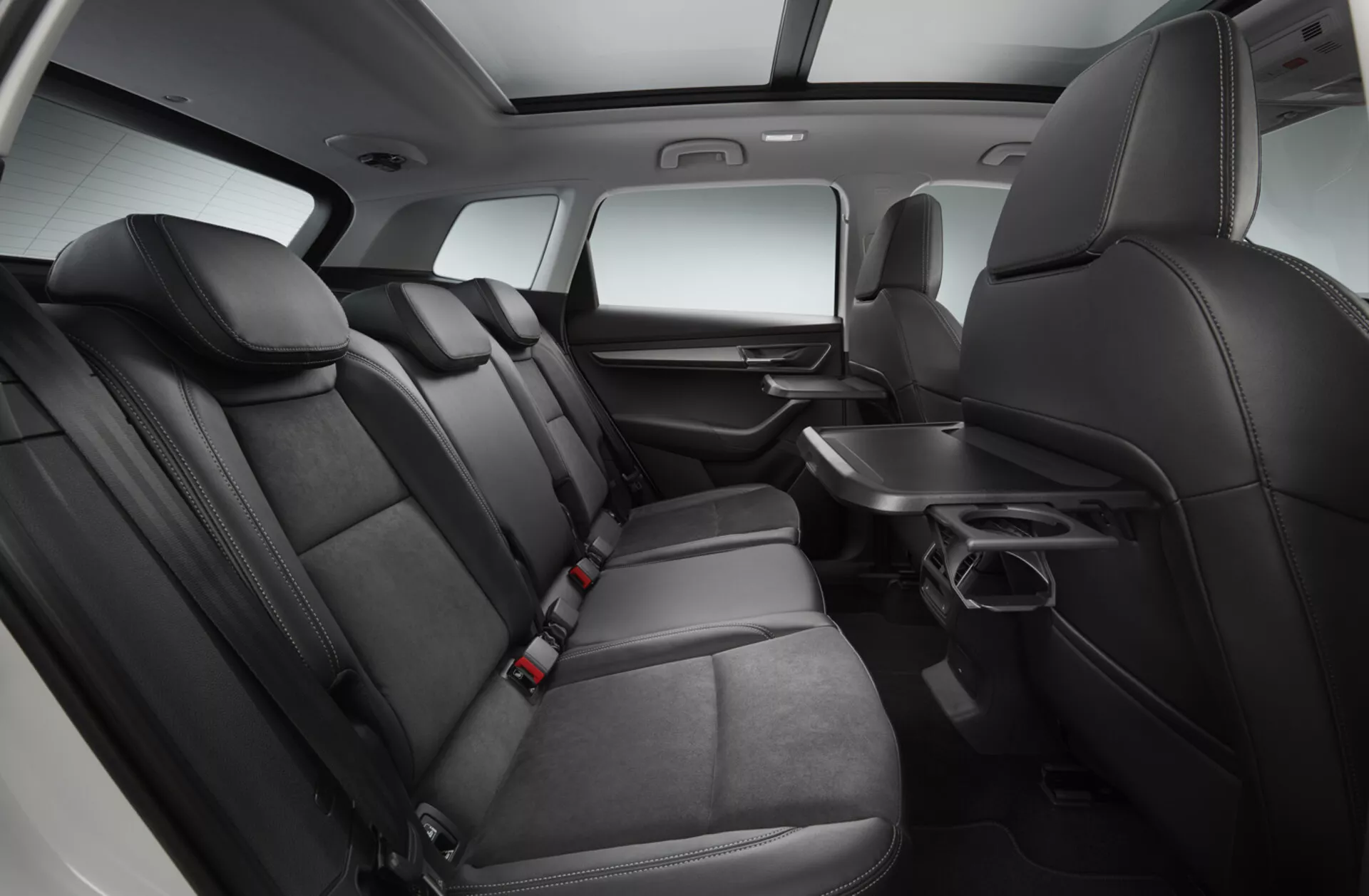 Vue intérieure d'une Skoda Karoq 2017 se concentrant sur la zone de sièges de la deuxième rangée avec des sièges en cuir noir haut de gamme, accoudoir rabattable avec porte-gobelets, panneau de porte avec commandes électriques, poches de rangement derrière les sièges avant, ceintures de sécurité pour toutes les positions, et une console centrale s'étendant à la deuxième rangée, le tout sous un éclairage de studio rehaussé