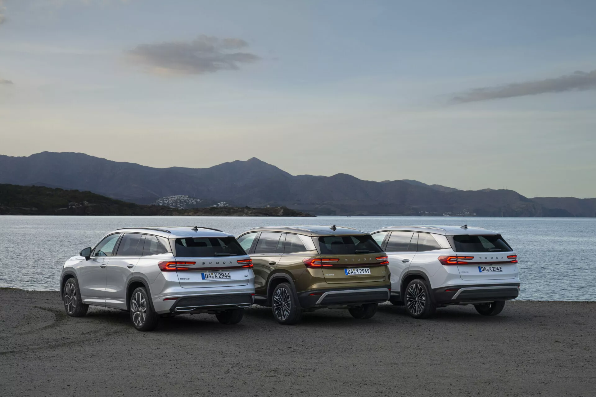 Gamme de Skoda Kodiaq 2024 avec trois SUV stationnés au bord de l'eau au crépuscule, montrant les profils arrières et l'esthétique du design devant un paysage doucement éclairé