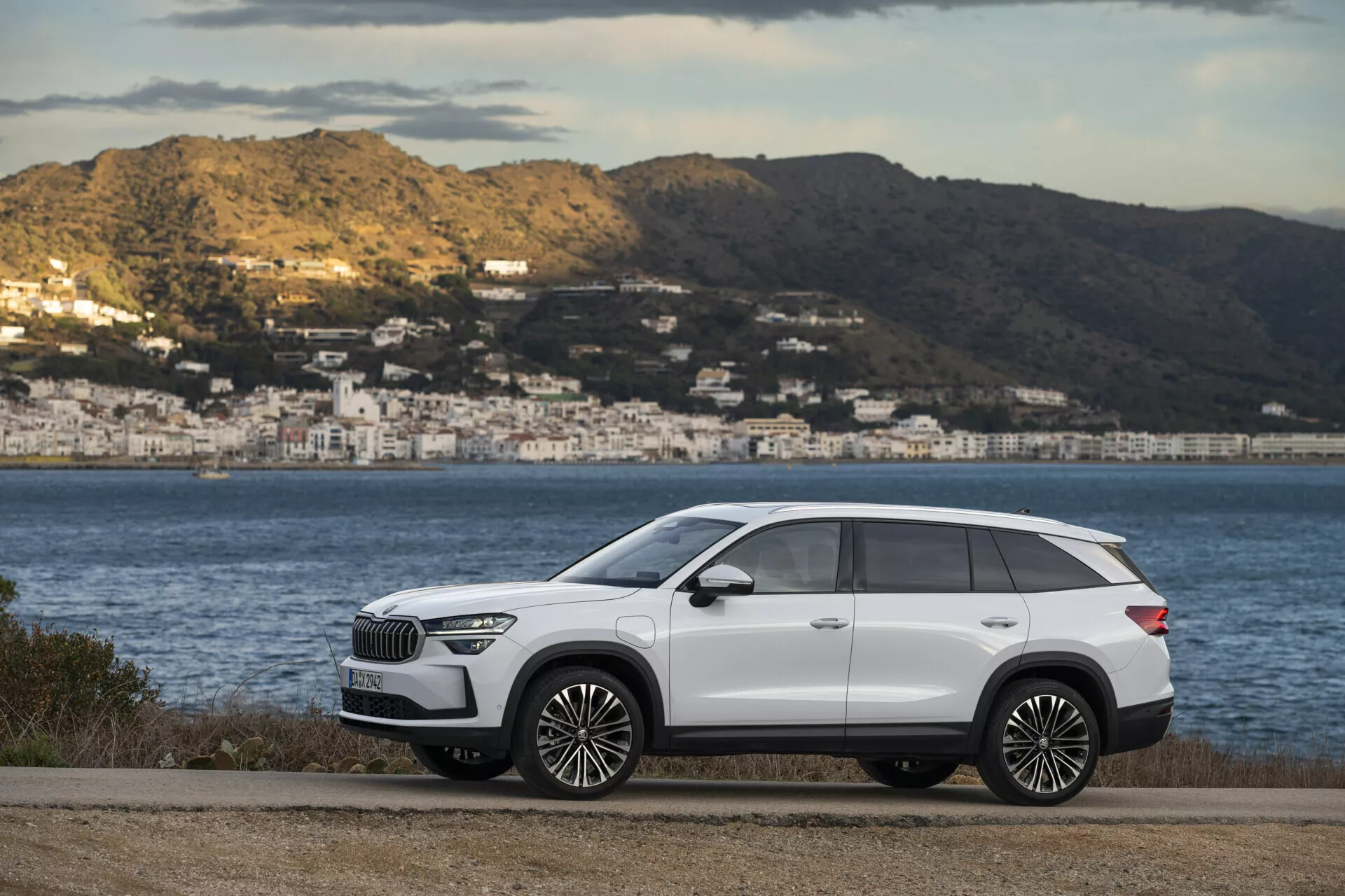 SUV premium Skoda Kodiaq blanc 2024 garé sur une route plate avec un paysage côtier en arrière-plan, montrant le profil latéral élégant du véhicule avec des détails chromés et des grandes jantes en alliage