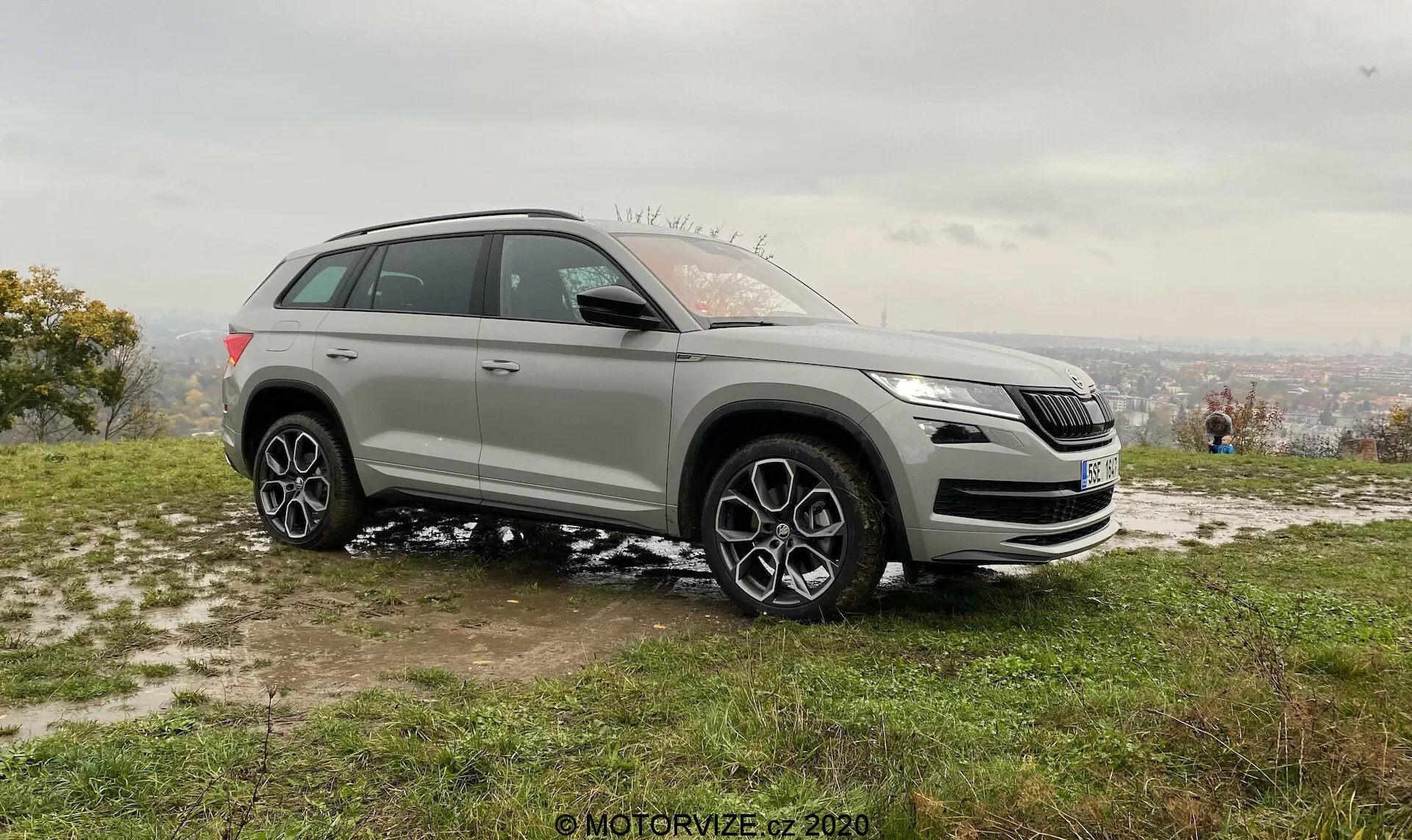 Vue de profil d'un SUV moderne prise sous un angle oblique montrant à la fois les éléments de design avant et latéral, dans un cadre naturel depuis un point de vue élevé. L'image met en évidence la calandre avant, les phares, les feux antibrouillard et le logo distinctif du véhicule. Elle montre également une grande garde au sol, de grandes roues en alliage à plusieurs branches, des arches de roue prominentes, une ligne d'épaule haute, des rétroviseurs latéraux, des barres de toit et des vitres teintées. Le design sportif et les technologies avancées potentielles du véhicule sont accentués dans cette prise de vue diurne stationnaire avec des plaques de neige, indiquant une saison plus froide.