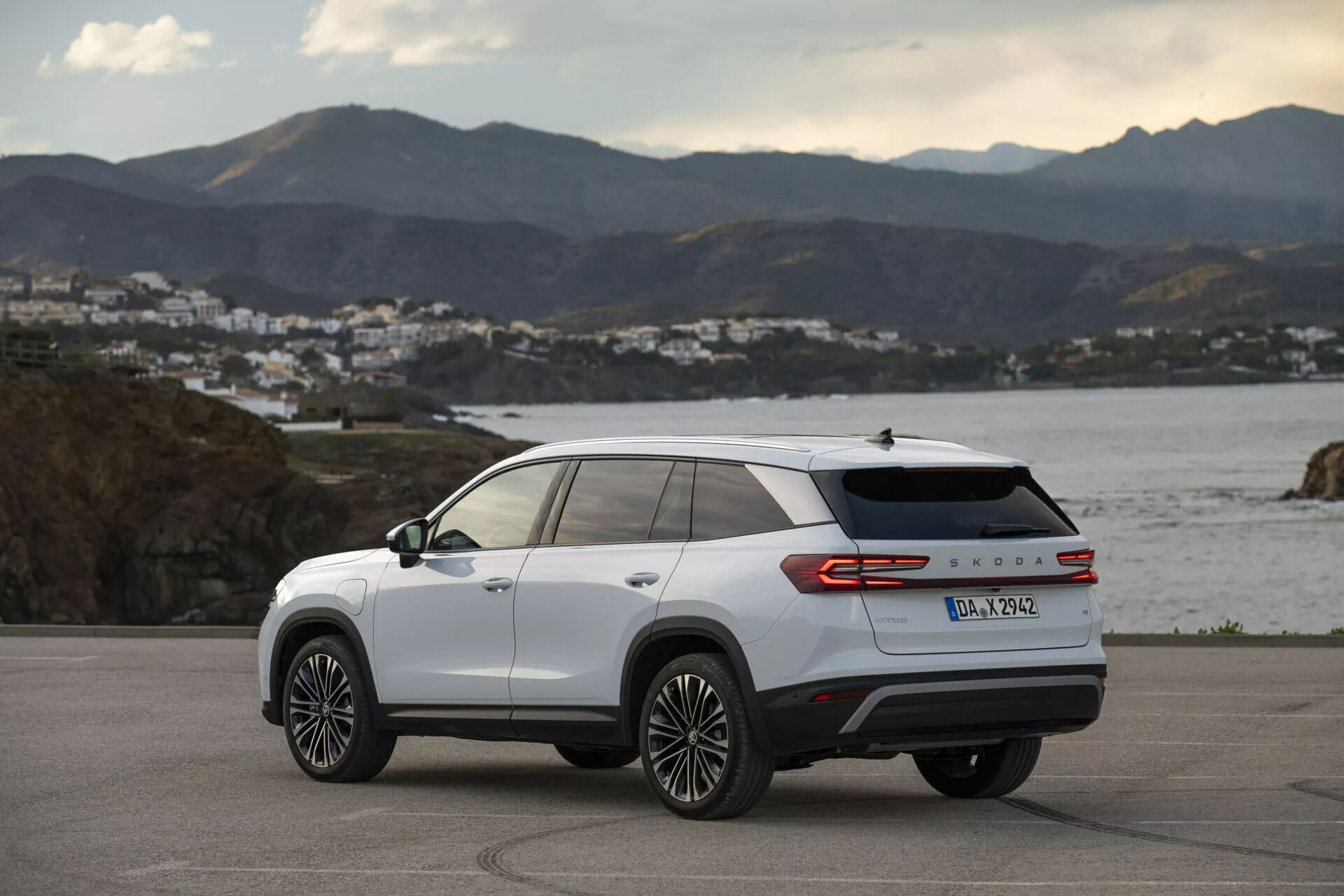 Vue arrière trois quarts d'un Skoda Kodiaq 2024 en blanc, montrant les lignes de conception latérale et arrière, jantes en alliage à multi-rayons, feux arrière LED et badge du modèle, garé à l'extérieur sur une route côtière à l'heure dorée