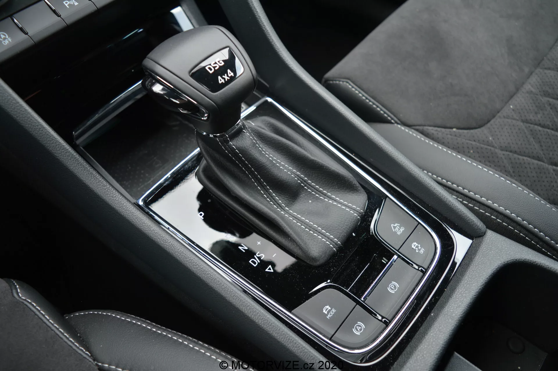 Vue rapprochée du levier de vitesses automatique et de la console centrale noire brillante de la Skoda Kodiaq 2017, avec modes de conduite, frein de stationnement électronique et bouton de maintien automatique; souligne les coutures en cuir sur le levier avec le mode sport.