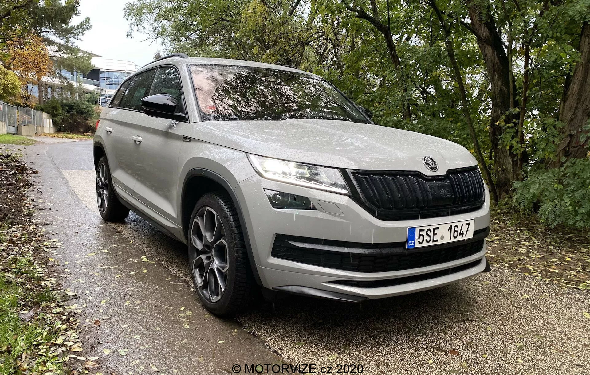 Skoda Kodiaq 2017 SUV moderne d'une marque automobile européenne, prise de vue frontale trois quarts affichant le profil avant et latéral jusqu'au milieu de la porte arrière, garée le long d'un chemin bordé d'herbe et d'arbres dans un environnement urbain ou suburbain. Les caractéristiques incluent une grille avant caractéristique avec des lamelles verticales, des phares à LED élégants, des feux antibrouillard dans le pare-chocs, de grandes entrées d'air sur le pare-chocs avant, des lignes de contour sur le capot pour l'aérodynamisme, des passages de roue proéminents avec des jantes en alliage à rayons multiples, des rétroviseurs avec clignotants intégrés, des moulures protectrices sur le bas de la carrosserie, et une peinture globalement propre et bien entretenue.