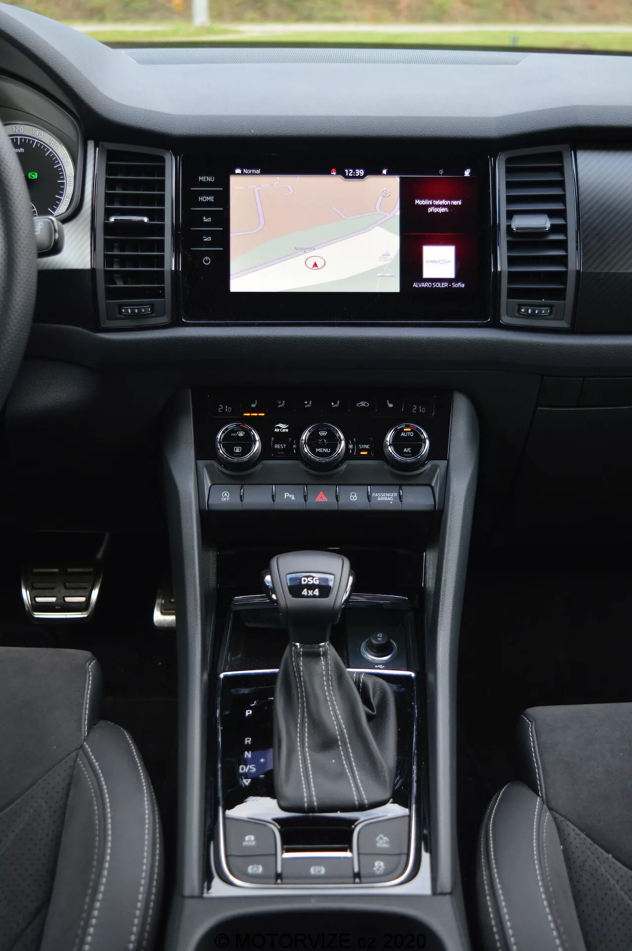 Vue intérieure d'une Skoda Kodiaq 2017 présentant la console centrale, le système d'infodivertissement à écran tactile affichant une carte, les molettes de contrôle climatique double, le levier de vitesses, le sélecteur de mode de conduite, les porte-gobelets, les sièges en cuir avec surpiqûres contrastantes et le bouton de démarrage sans clé