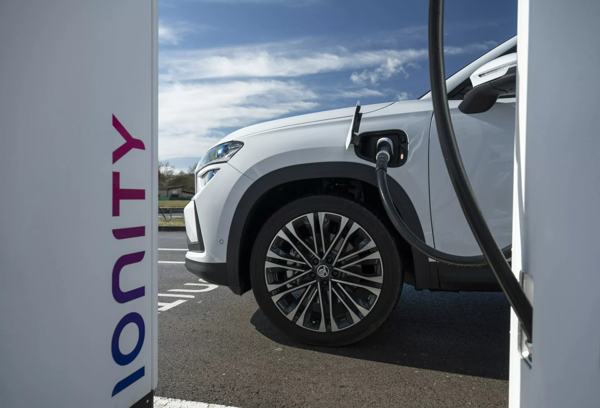 Vue de côté en gros plan d'une Skoda Kodiaq électrique blanche 2024 en charge à une station Ionity, illustrant la technologie de charge rapide et un design moderne