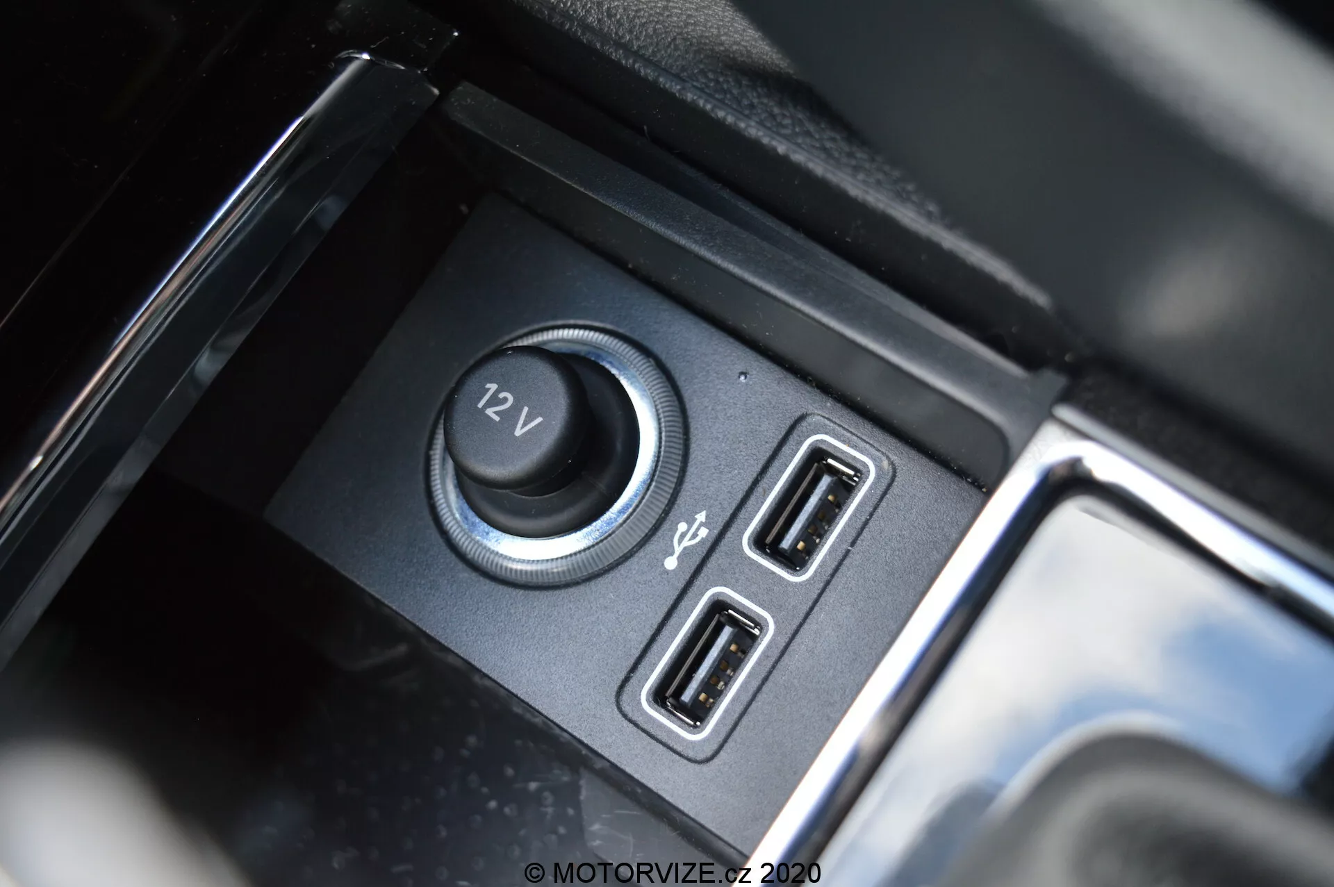 Gros plan de l'intérieur de la Škoda Kodiaq 2017 mettant en avant les fonctionnalités d'alimentation et de connectivité, y compris une prise de courant 12V et des ports USB doubles, avec un compartiment noir mat et des accents réfléchissants brillants.
