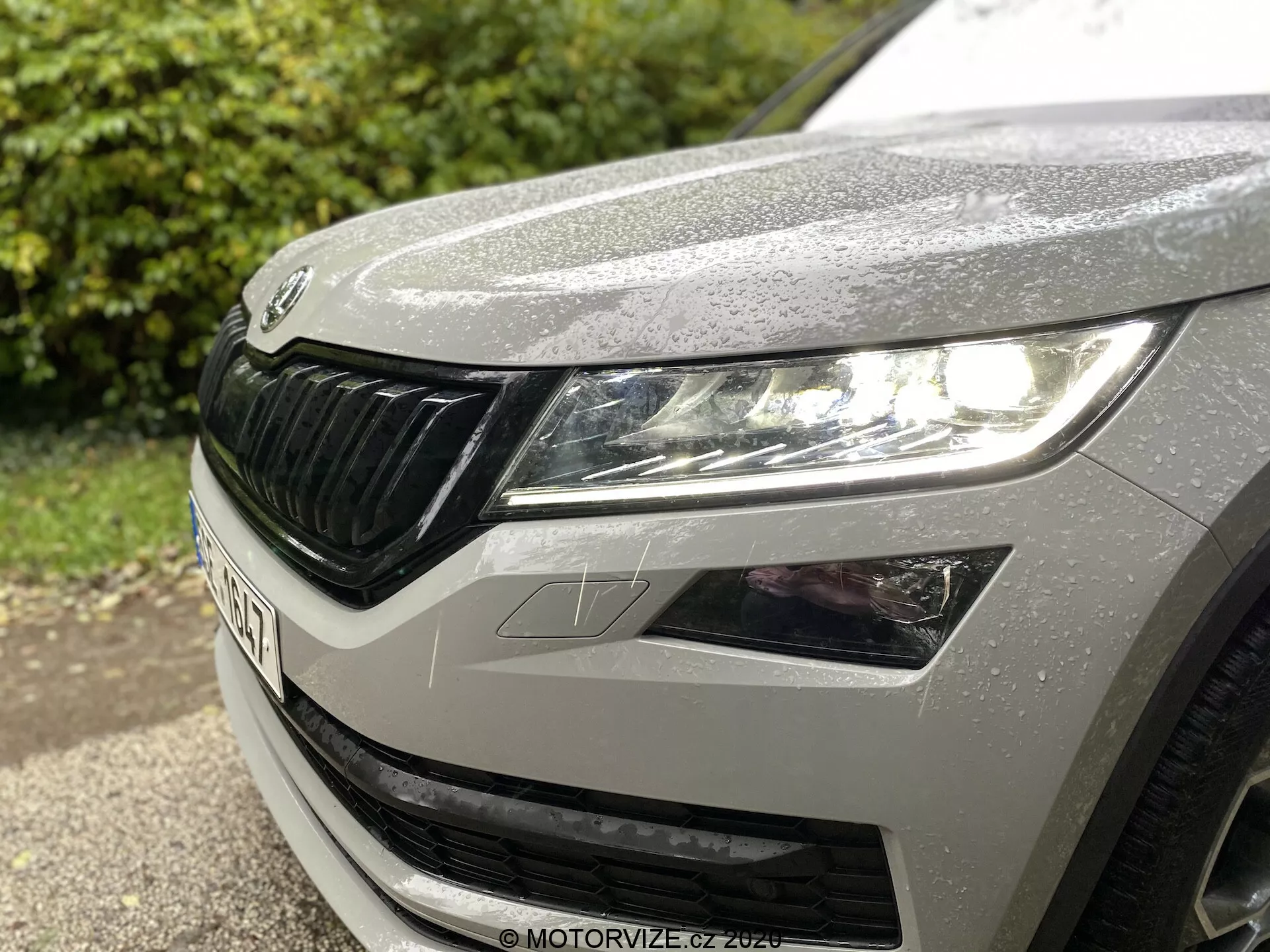 Vue rapprochée du quart avant-gauche d'une Škoda Kodiaq 2017, mettant en avant le phare gauche au design moderne LED, une partie du capot avec des gouttelettes de pluie et la grille distinctive de Škoda avec des éléments horizontaux.