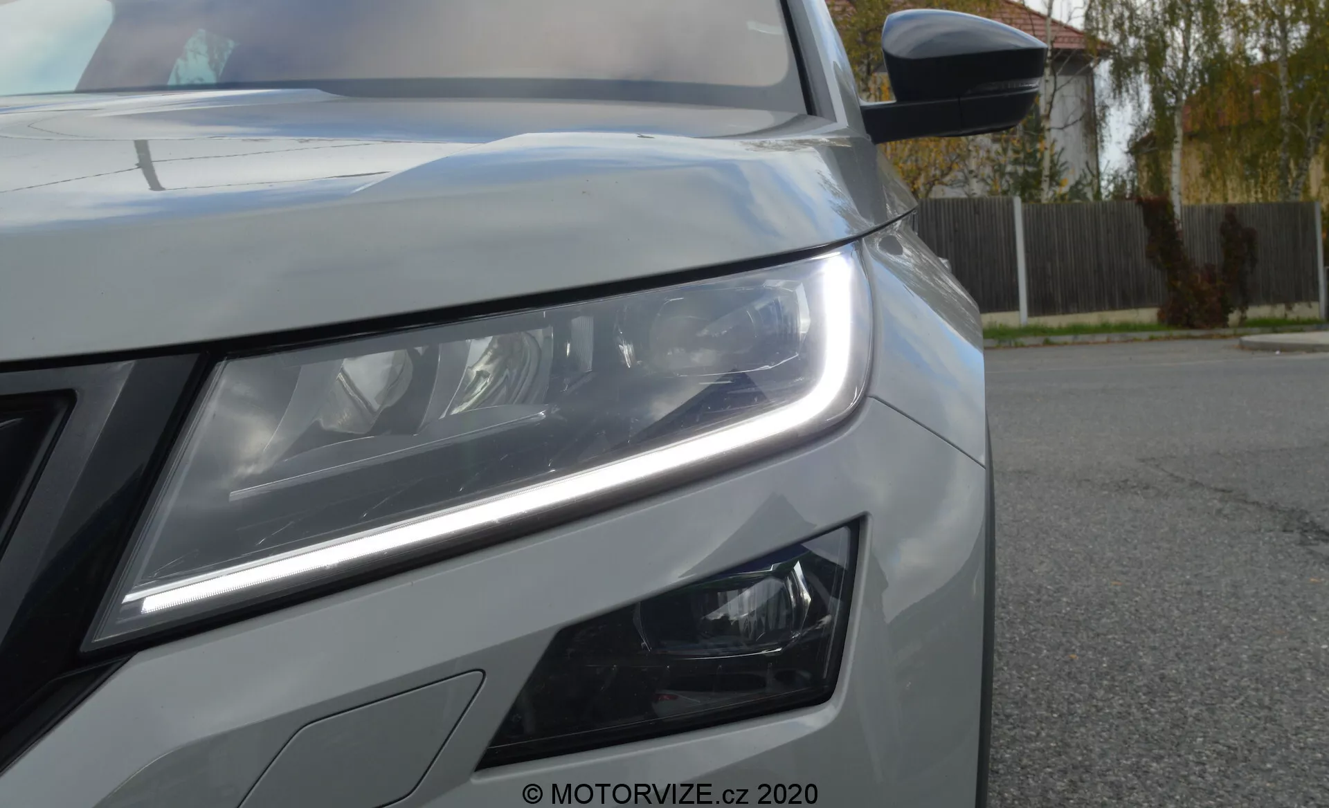 Vue en gros plan du côté avant gauche d'une Skoda Kodiaq 2017. La perspective en angle bas met en valeur les feux de jour à LED distinctifs et les phares principaux détaillés suggérant une technologie d'éclairage avancée. Des phares antibrouillard au design moderne sont visibles sous le phare principal. L'image montre également une partie de la calandre avant, une peinture métallique avec des lignes de carrosserie nettes et un rétroviseur latéral avec clignotant intégré. Il y a un filigrane 'MOTORVIZE.cz 2020' indiquant la source de la photographie.