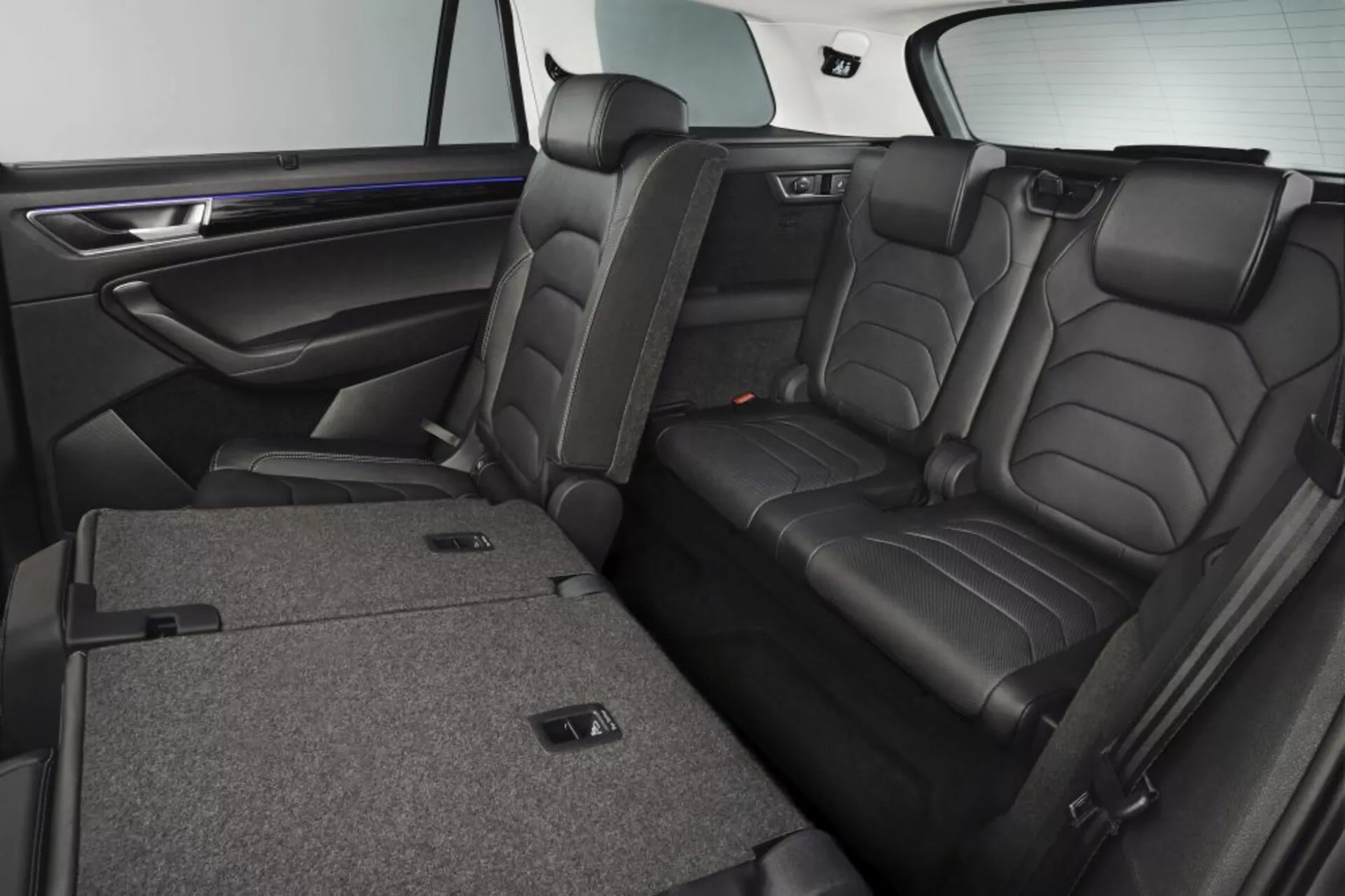 Intérieur du Skoda Kodiaq 2017 montrant des sièges arrière en cuir de luxe avec appuie-tête, fonction de pliage 60/40 pour agrandir l'espace de chargement, accoudoir central avec porte-gobelets, et garniture de porte effet bois premium avec éclairage d'ambiance