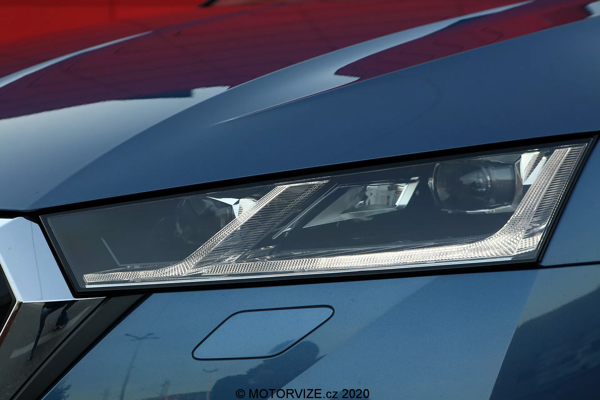 Une vue rapprochée du phare gauche du modèle limousine Škoda Octavia 2020, mettant en évidence son design angulaire et la technologie moderne d'éclairage LED ou laser. La photographie, prise sous un angle bas, montre les réflecteurs internes complexes et les détails fins dans le phare couvert d'une lentille claire. L'image haute résolution révèle également une partie du capot et de l'aile avec une finition de peinture métallique, suggérant un véhicule haut de gamme ou bien entretenu. Cette image met l'accent sur l'éclairage automobile avancé et le style agressif associé aux voitures de sport.