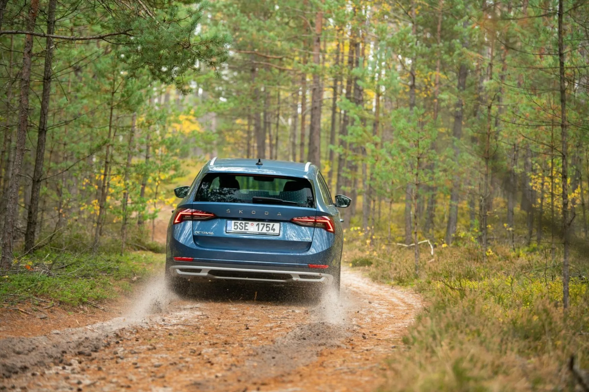 Limousine Skoda Octavia 2017 en bleu, présentant des feux arrières LED, essuie-glace arrière et double échappement sur un sentier forestier avec déplacement dynamique de terre indiquant des capacités de traction intégrale