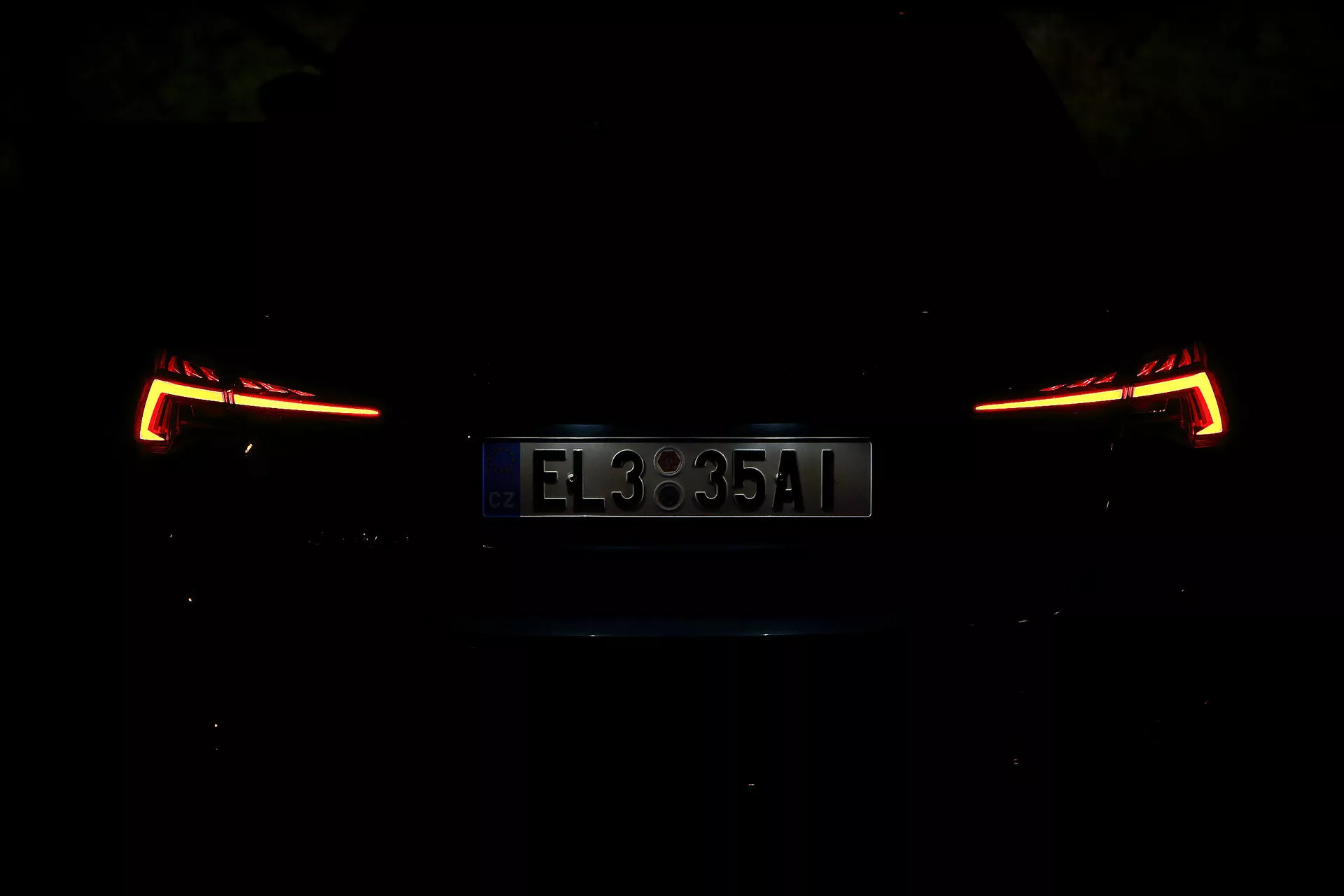 Vue arrière d'une Skoda Octavia 2020 Limousine, photographiée la nuit ou dans un environnement faiblement éclairé. L'image se concentre sur les feux arrière et la plaque d'immatriculation, mettant en valeur un design moderne et angulaire. Les détails de la voiture sont obscurcis en raison de la faible luminosité, soulignant la section arrière élégante et contemporaine.
