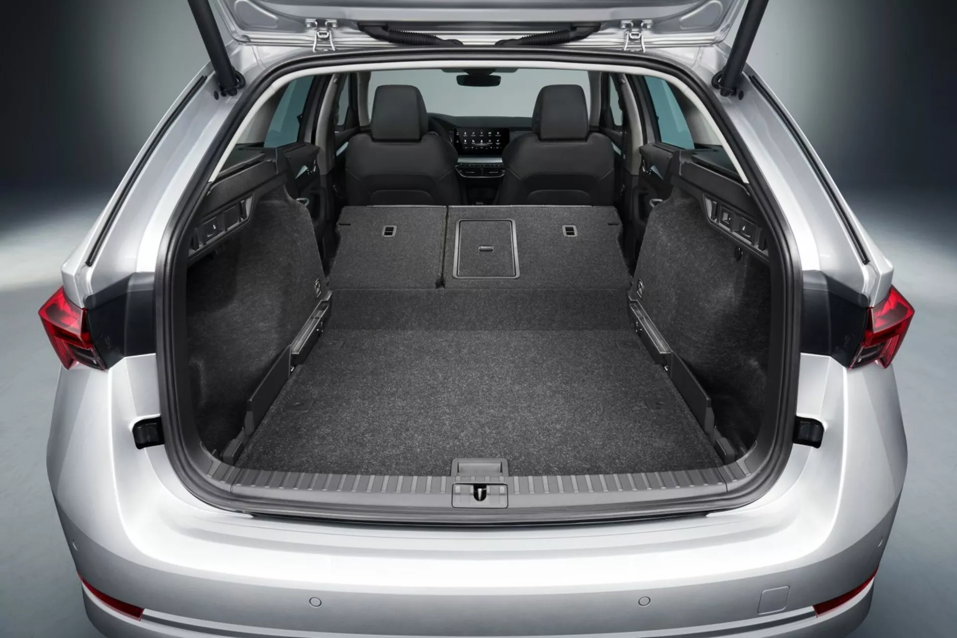 Coffre ouvert de la berline Skoda Octavia 2017 montrant un vaste espace de chargement avec sièges arrières repliés, sol plat, revêtement de moquette, points d'ancrage pour un stockage sécurisé, et possibles caractéristiques technologiques avancées telles que les lumières LED