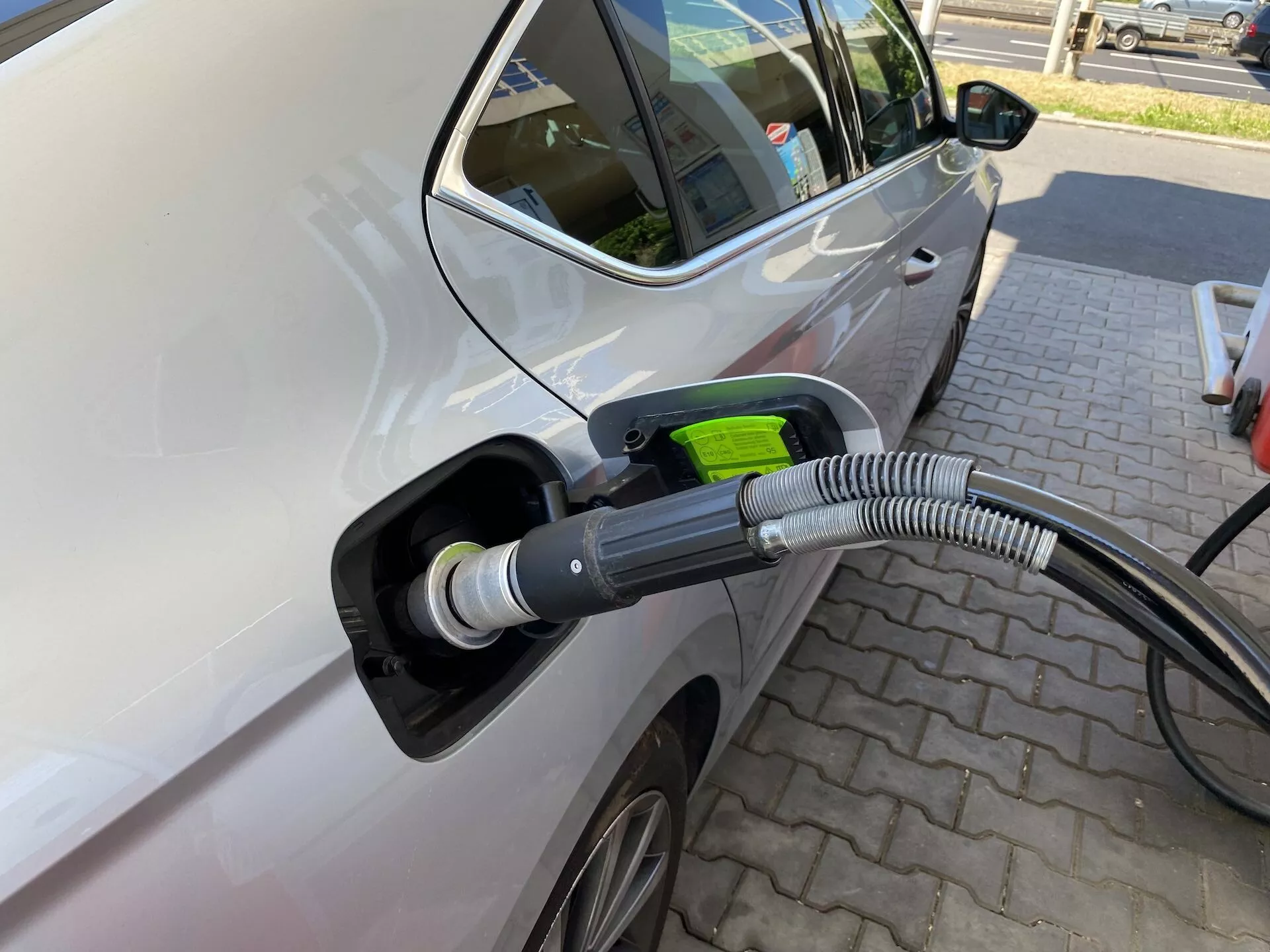 Vue en gros plan du côté gauche d’une Skoda Octavia 2020 connectée à une station de recharge électrique, mettant en évidence la zone du port de recharge avec un focus sur le câble et le port de recharge. L’image est prise sous un léger angle de l’avant vers l’arrière, montrant la porte du conducteur avant et une partie de la porte arrière, indiquant un véhicule à plusieurs portes. Les caractéristiques comprennent un rétroviseur latéral moderne, une roue en alliage partiellement visible, une couleur de voiture claire avec une finition brillante, un port de recharge ouvert avec une couverture protectrice épaisse et ondulée sur le câble et une poignée de prise de couleur verte symbolisant la respectabilité de l’environnement. La voiture est garée sur une zone pavée avec des motifs de briques, suggérant une station de recharge dédiée, sans autres véhicules à proximité, mettant en avant l’action de recharge.