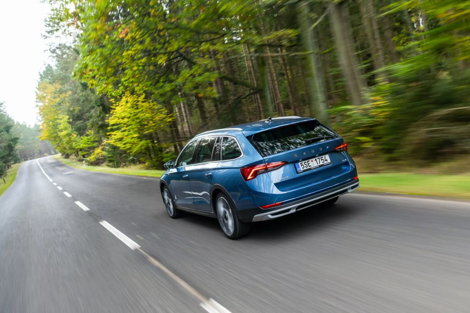 Skoda Octavia break 2017 en mouvement, capturée sous un angle arrière de trois quarts mettant en valeur le design aérodynamique, le coffre hayon arrière et les feux arrière horizontaux sur une route bordée de forêts