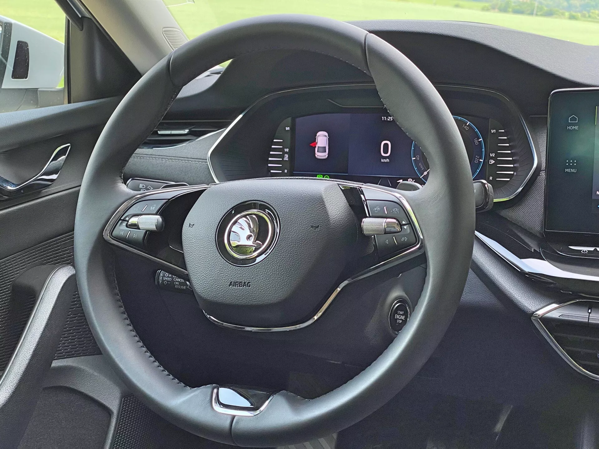 Intérieur de la Skoda Octavia Limousine 2020 depuis la perspective du conducteur, en mettant en avant le volant moderne à trois branches en cuir avec divers contrôles pour le volume, les commandes vocales et les réglages du régulateur de vitesse. Le tableau de bord entièrement numérique derrière le volant affiche un compteur de vitesse fixe et un indicateur de portes ouvertes. La console centrale dispose d'un écran tactile pour l'infodivertissement, la navigation et les réglages du véhicule. Le tableau de bord montre un design moderne avec des matériaux de haute qualité.