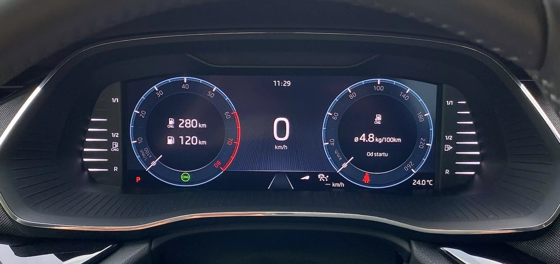 Vue rapprochée du tableau de bord numérique de la Skoda Octavia 2020 depuis la perspective du conducteur, avec un écran large à fond noir et des graphismes numériques vibrants. Sur le côté gauche se trouve un tachymètre jusqu'à 8 000 tr/min avec zone rouge à 6 500 tr/min et l'aiguille au ralenti. Au centre est affichée une vitesse de '0 km/h', une horloge à '11:29', une consommation de carburant de '4,8 l/100km' et une distance de '6540 km'. Sur le côté droit, un graphique ressemblant à un compteur de vitesse avec des marques jusqu'à 280 km/h et une température de '24°C'. Les icônes incluent une boussole de navigation et une jauge de carburant.