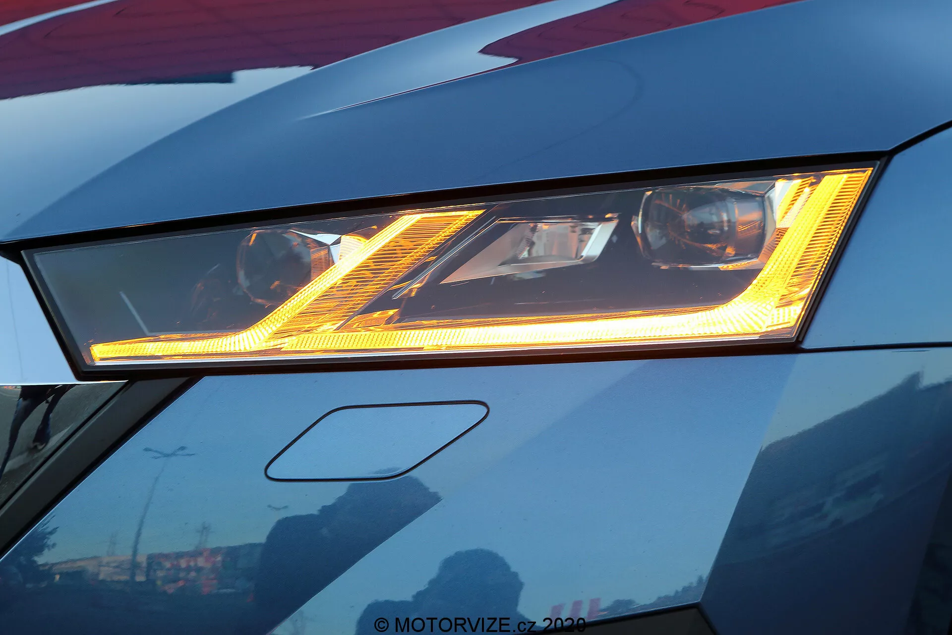 Gros plan sur le phare à LED avancé d'une Skoda Octavia 2020 rouge foncé, mettant en évidence son illumination brillante et ses motifs lumineux distinctifs. Le design sophistiqué comporte une lumière de jour (DRL) sous le phare principal, la carrosserie élégante affichant des arêtes vives. Les reflets du ciel et des bâtiments sur la surface bien polie suggèrent une finition premium. Le cadrage révèle légèrement le pare-chocs avant, se concentrant sur l'innovation du design automobile.