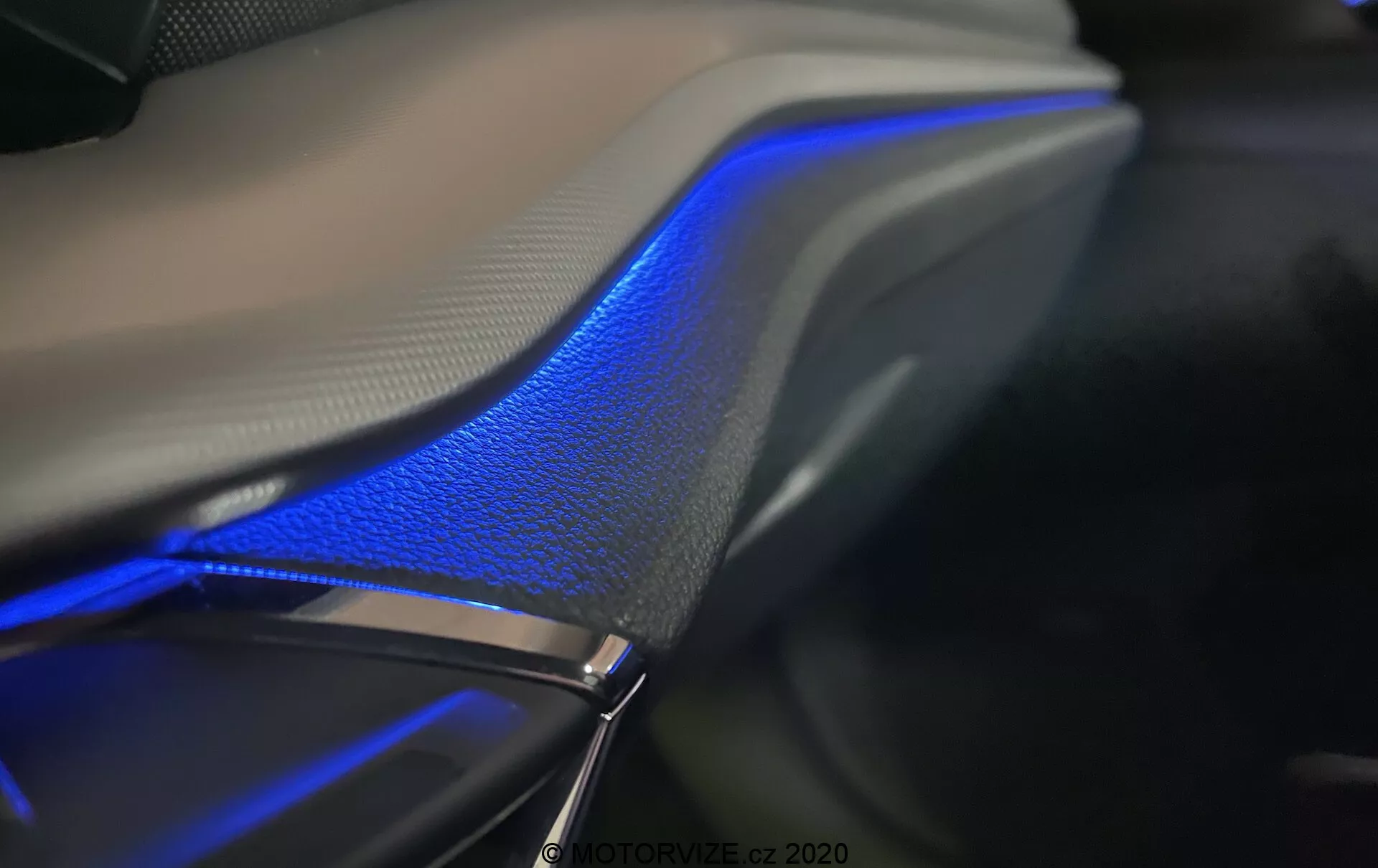 Détail intérieur en gros plan de la Skoda Octavia Limousine 2020, mettant en valeur la bande lumineuse ambiante bleue qui longe la porte ou le tableau de bord de la voiture. Le design élégant aux courbes douces se fond parfaitement avec la surface en cuir, soulignant la sensation de luxe sous l'éclairage doux. Pris dans un environnement sombre, la photographie accentue l'éclairage bleu et les textures des matériaux, montrant la technologie de l'éclairage ambiant souvent contrôlée via le système d'infodivertissement du véhicule.
