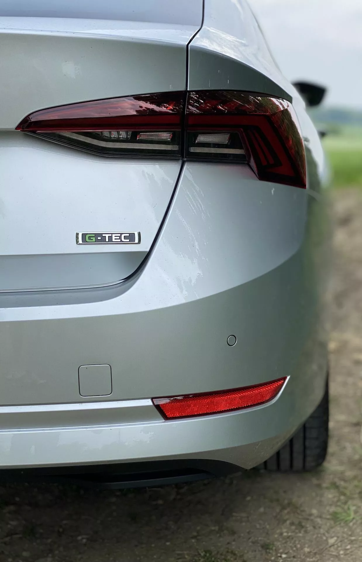 Vue oblique en gros plan de la section arrière droite d'une Skoda Octavia Limousine 2020 argentée. L'image met en évidence le feu arrière, l'insigne G-TEC, le design élégant du coffre, le pare-chocs arrière, le réflecteur arrière et la finition de peinture métallique. L'arrière-plan flou met en valeur les caractéristiques de design de la voiture.