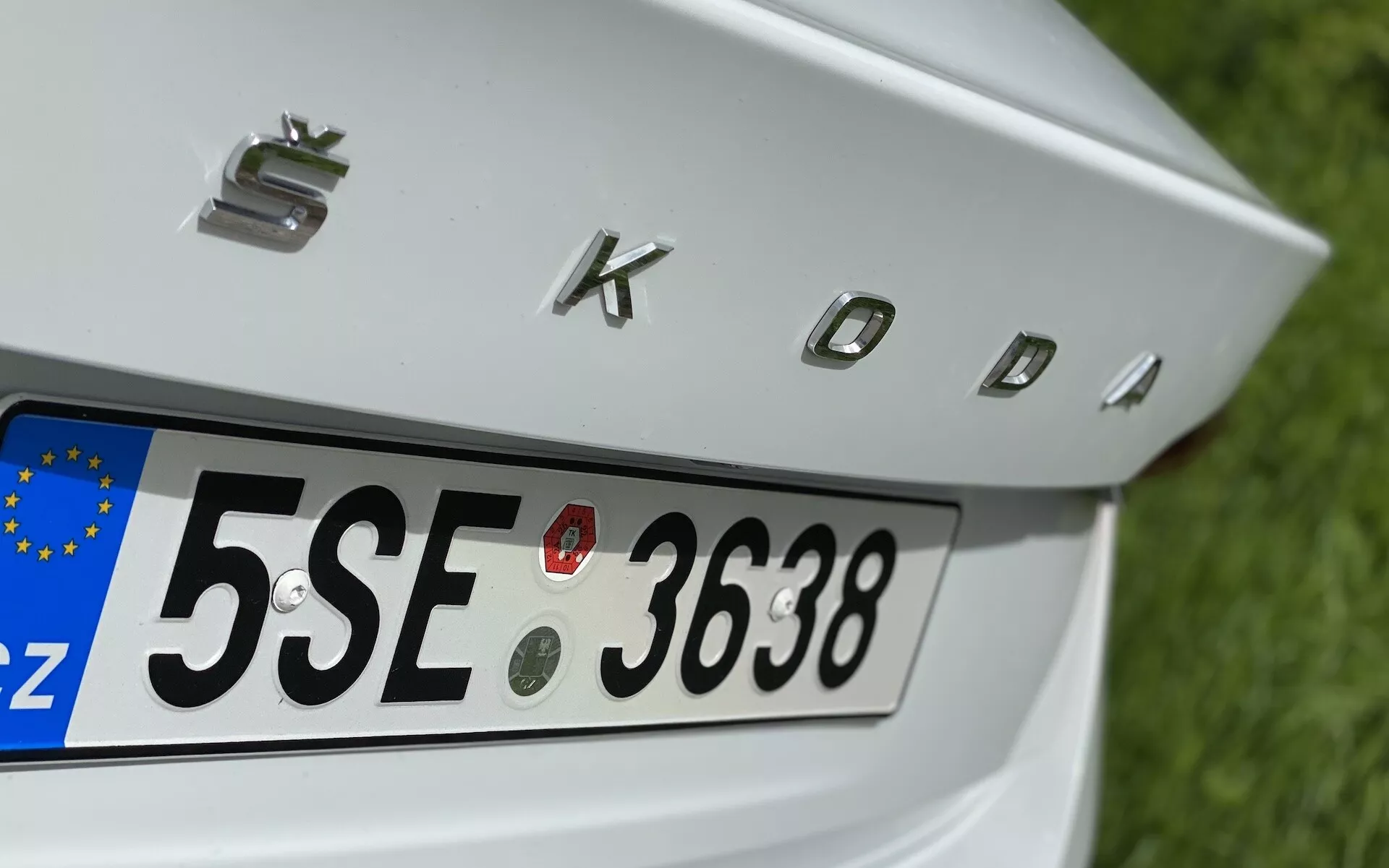Vue arrière partielle en gros plan de la Škoda Octavia 2020 limousine, centrée sur le couvercle du coffre, la plaque d'immatriculation arrière avec identifiant européen 'CZ' et les lettres chromées 'SKODA'. Inclus, quatre capteurs de stationnement circulaires au-dessus de la plaque pour l'assistance à la manœuvre.