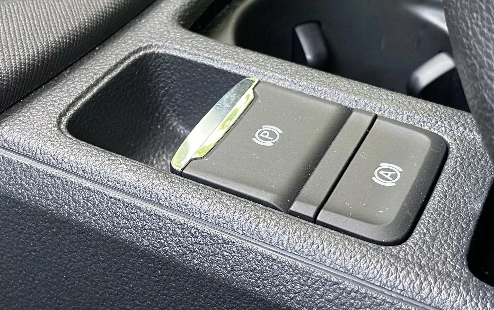 Vue rapprochée du panneau de commande de la Skoda Octavia 2020 à l'intérieur du véhicule, montrant les boutons des sièges chauffants et ventilés sur un matériau sombre, granuleux et ressemblant à du cuir. Le bouton gauche présente une icône de siège chauffant et le bouton droit affiche une icône de siège ventilé, avec un petit indicateur LED entre les boutons.