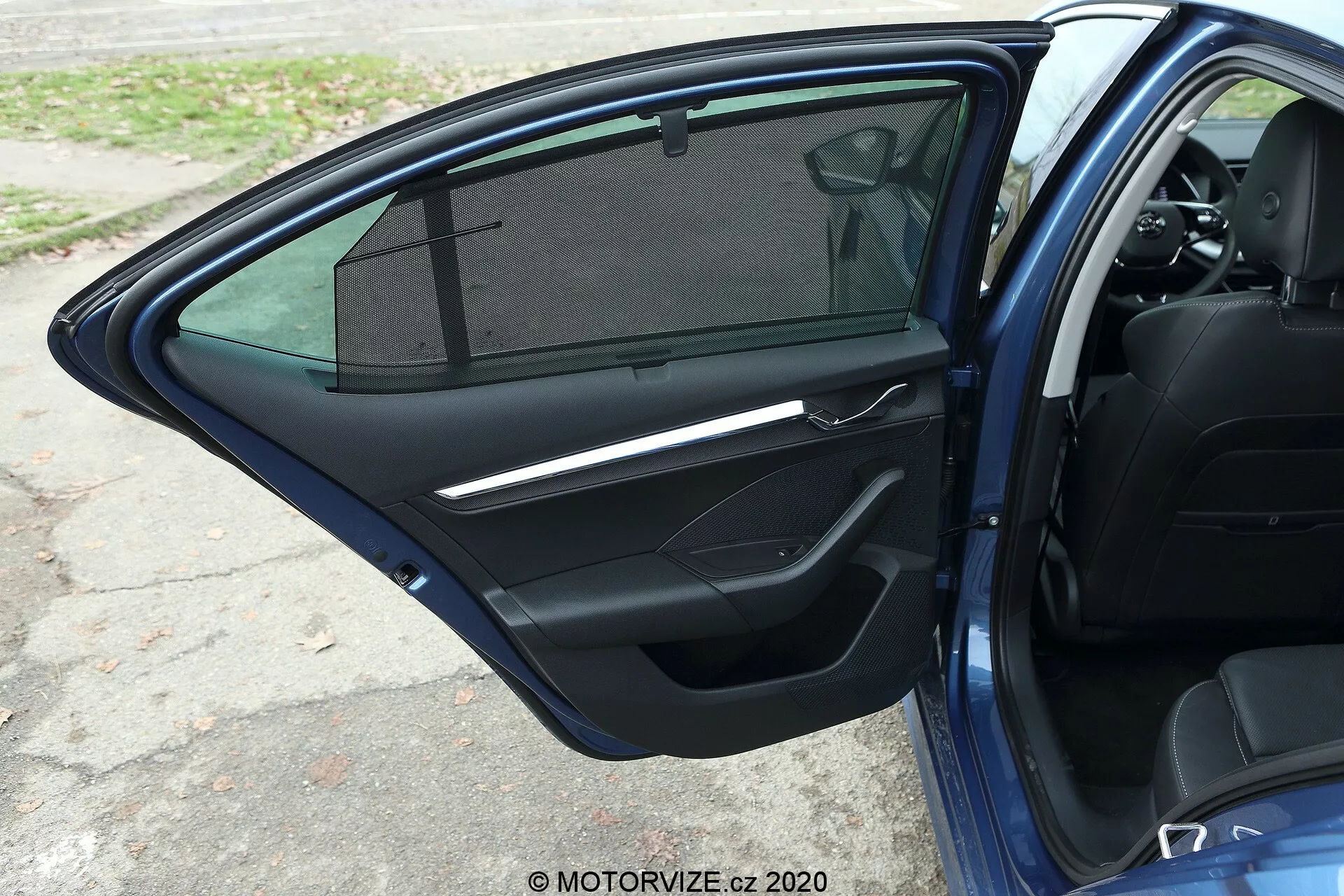 Vue rapprochée de la porte passager avant ouverte de la Skoda Octavia 2020 limousine, mettant en évidence un panneau de porte intérieur de couleur sombre avec poignée métallique, panneau de commande pour les vitres électriques, compartiment de rangement, grille de haut-parleur, seuil de porte partiellement visible et fenêtre avec pare-soleil.