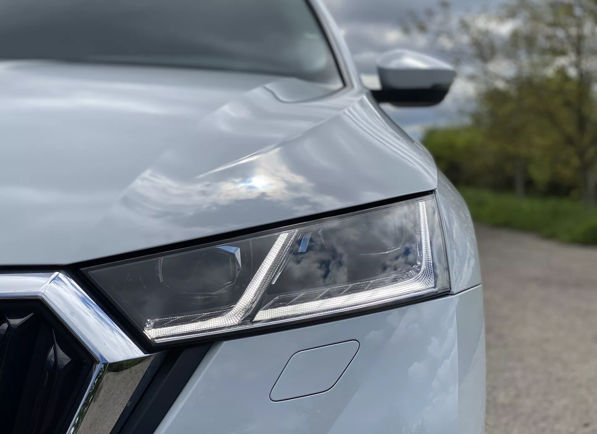 Vue rapprochée de la Skoda Octavia Limousine 2020, mettant en avant l'assemblage complexe du phare avant gauche avec éléments LED et feux diurnes. Une partie de la calandre avant avec des contours en chrome est visible, ainsi que le capot de la voiture avec des courbes aérodynamiques, créant un aspect moderne et stylé indiquant une technologie et un design premium.