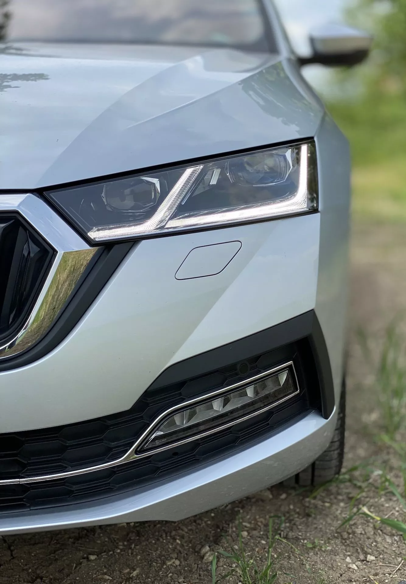 Gros plan de la section avant gauche de la Skoda Octavia 2020 (Octavia Limousine) présentant des détails du centre de la grille au phare gauche, une partie du capot et une portion du pare-chocs avant et de l'aile. L'image, prise sous un angle bas, met en évidence le design élégant du phare avec des feux de jour LED, la grille encadrée par des accents chromés et la grille inférieure avec sa finition métallique moderne. La mise au point est sur les détails de la voiture avec une faible profondeur de champ, créant une apparence professionnelle et de haute qualité.