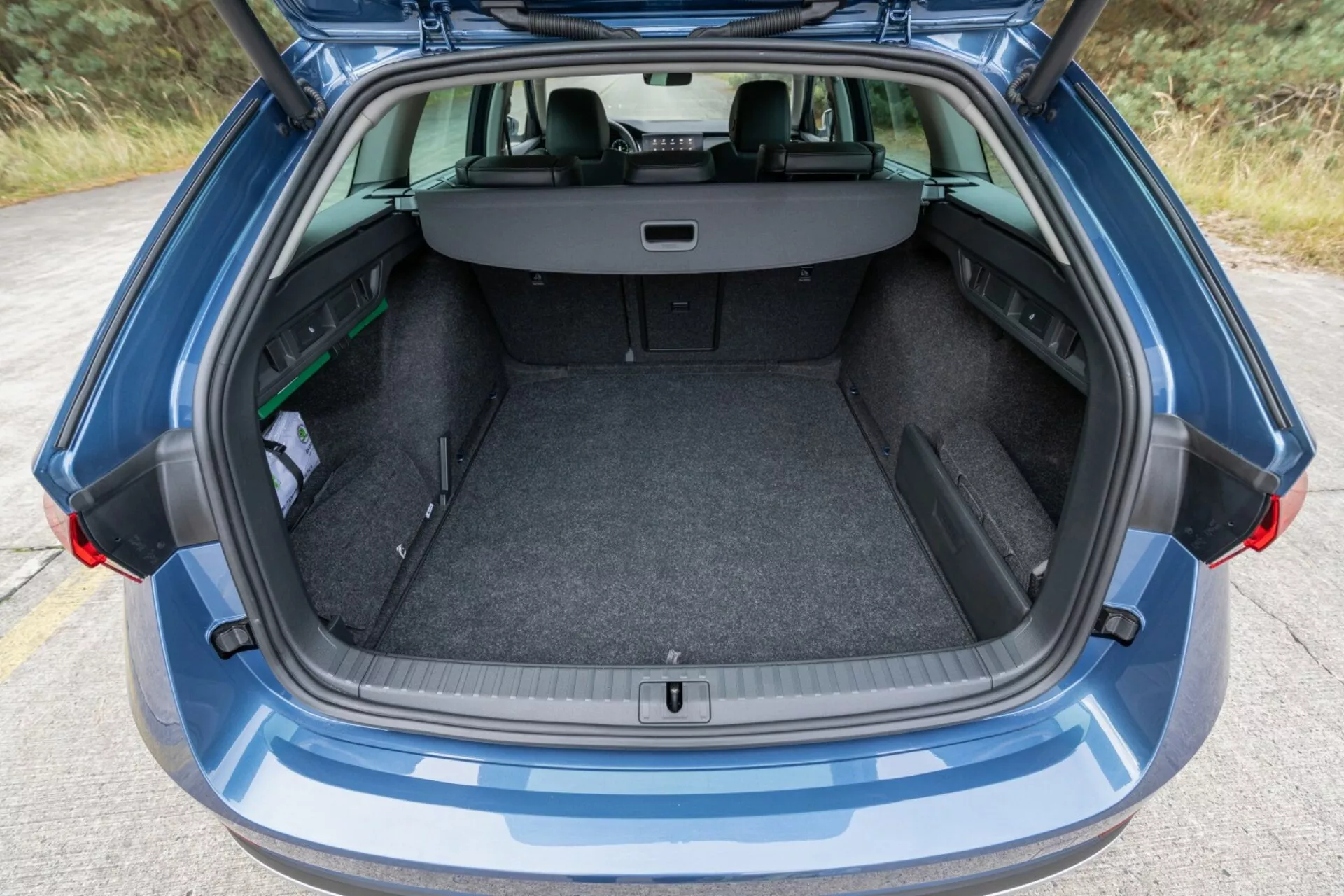 Vue arrière d'une Skoda Octavia Limousine 2017 mettant en évidence son espace de coffre spacieux et propre avec hayon ouvert, couvercle de chargement rétractable et sièges arrière visibles en configuration divisée 60/40 pour une capacité de chargement étendue, à côté d'un petit parapluie et d'un objet vert, sous une lumière ambiante.