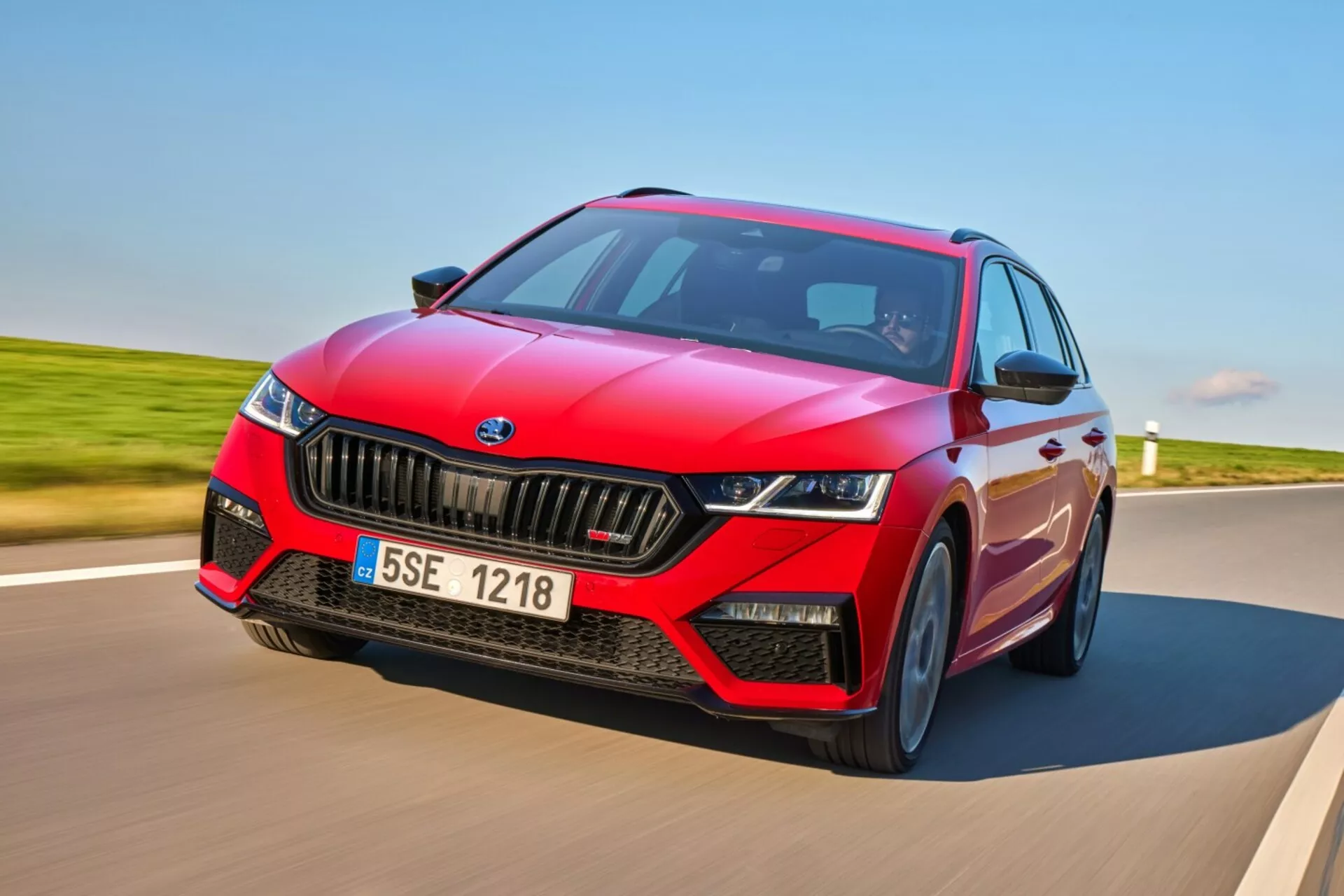 Skoda Octavia RS hatchback 2017 en mouvement dynamique sur une route pavée, présentant un design sportif rouge avec accents noirs, phares LED, et fonctionnalités technologiques avancées incluant l'ADAS et le toit panoramique