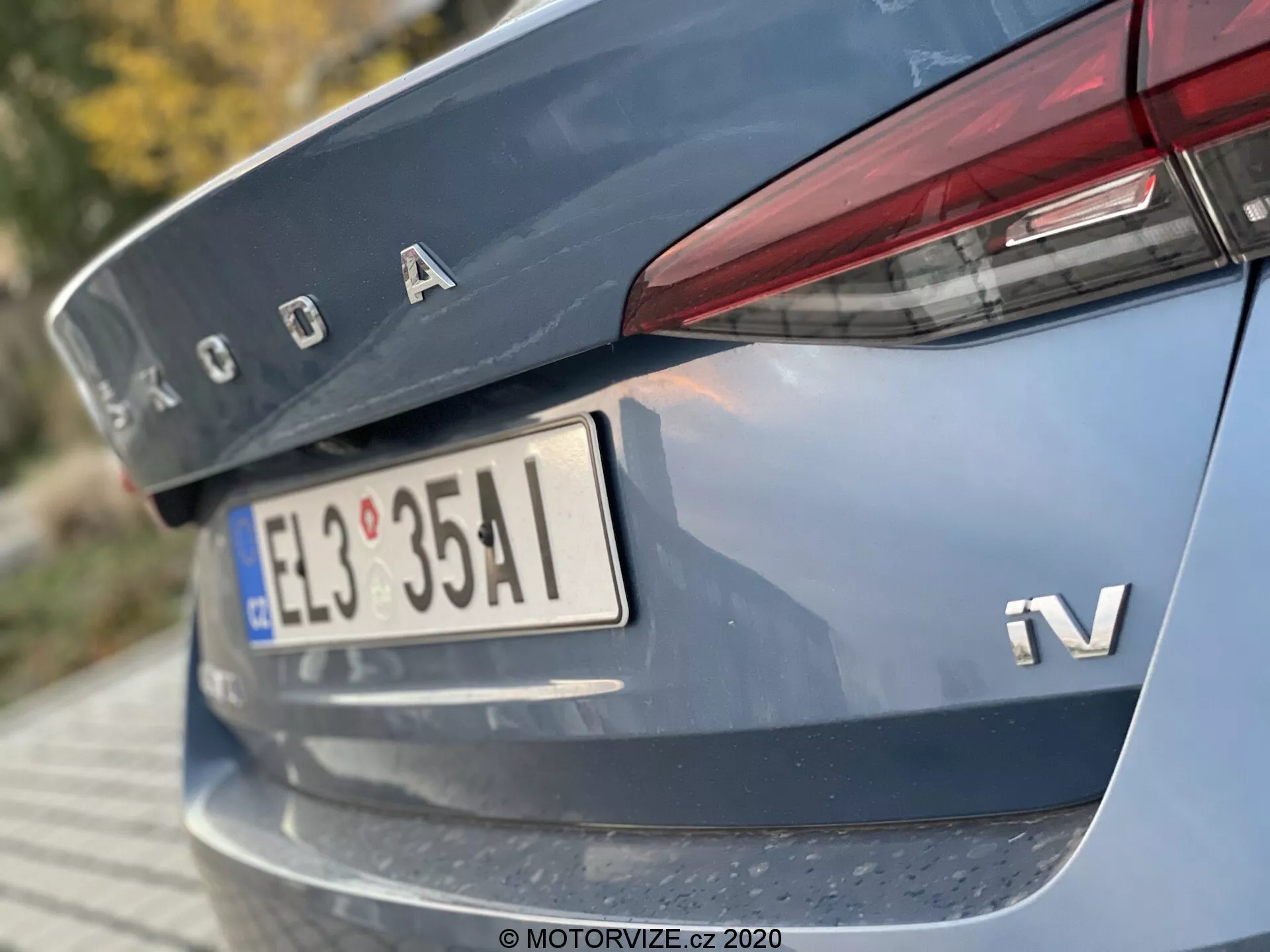 Gros plan sur la section arrière d'une Škoda Octavia Limousine 2020, pris sous un angle bas en se concentrant sur le couvercle du coffre, une partie du pare-chocs arrière, et comportant le logo en chrome Škoda, l'insigne iV pour la variante hybride ou électrique, la plaque d'immatriculation de style européen, des feux arrière étroits et horizontaux qui s'étendent à la portière du coffre, et une bande réfléchissante sur le pare-chocs arrière.